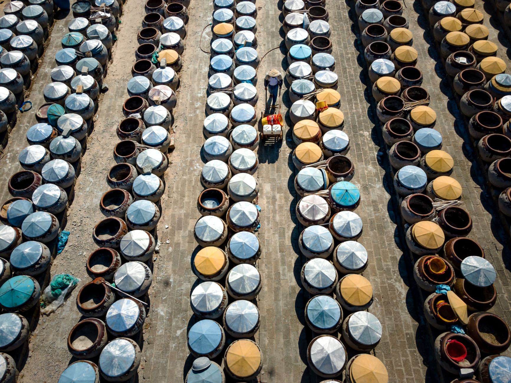 An aerial drone shot showing a person working among rows of fermentation containers outdoors.
