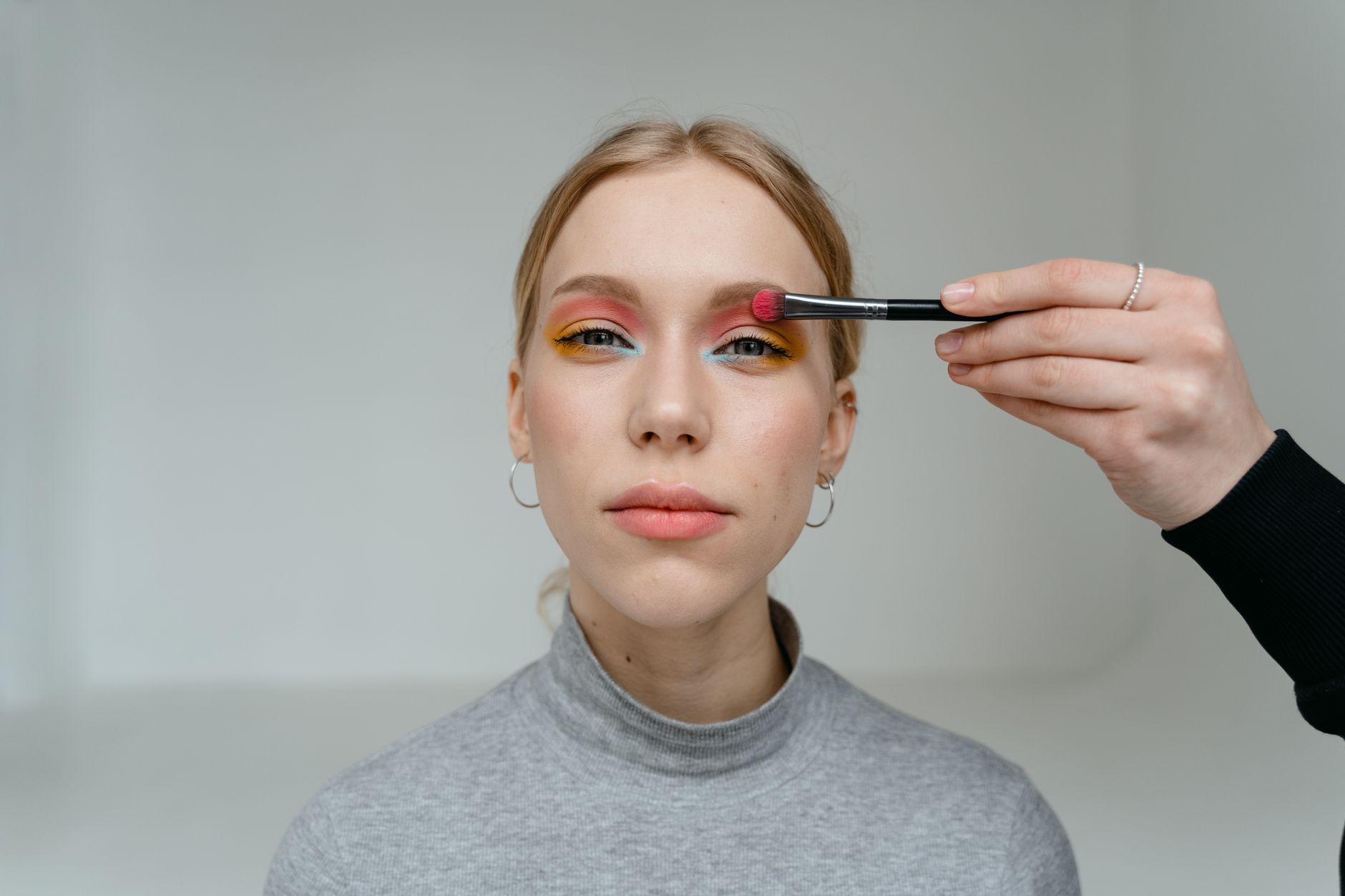 Close-up portrait of a woman having vibrant eyeshadow applied with makeup brush.
