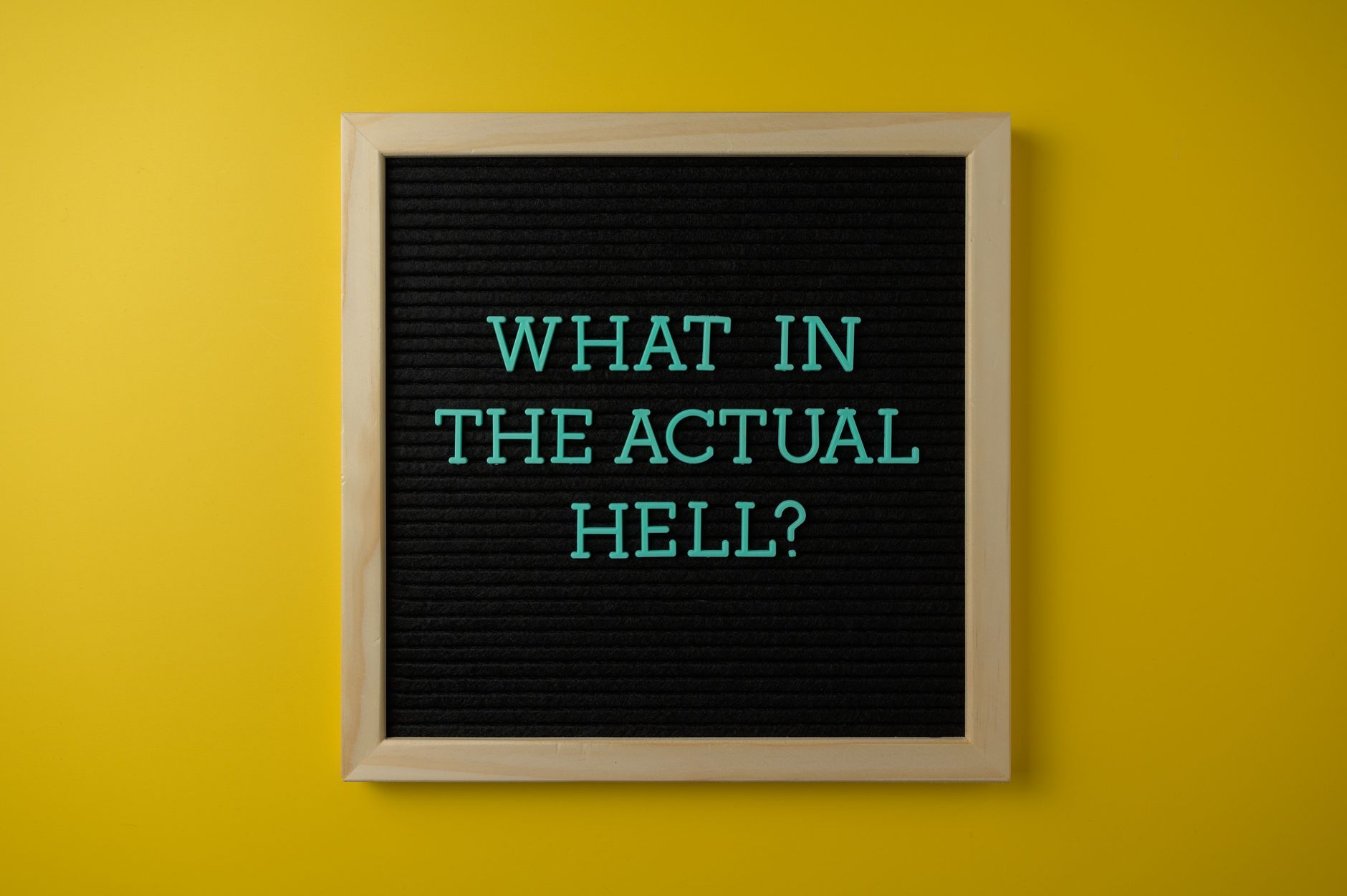 Letter board with humorous quote 'What in the actual hell?' on a vibrant yellow backdrop.
