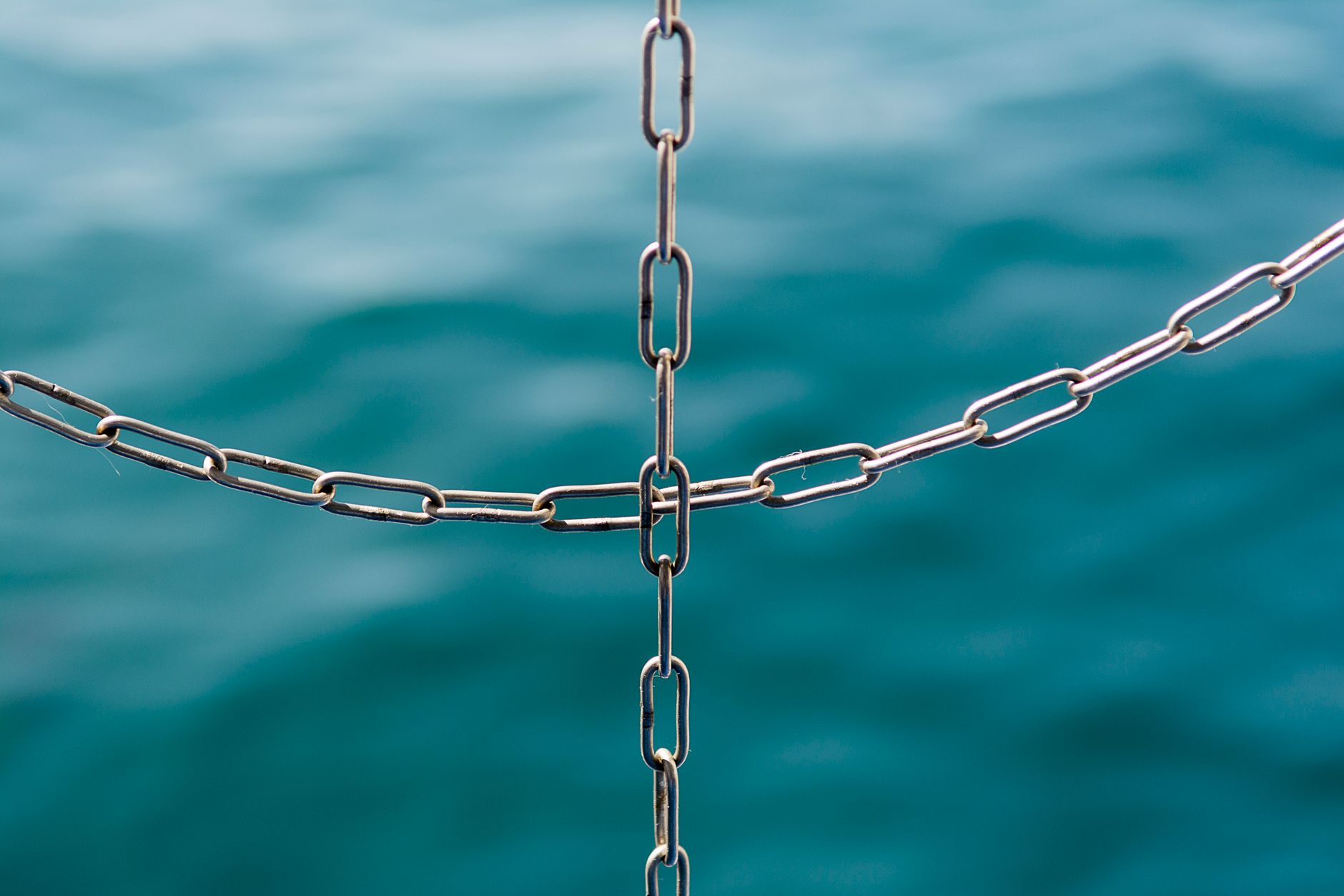 A symbolic close-up of intersecting metal chains over a serene sea background.