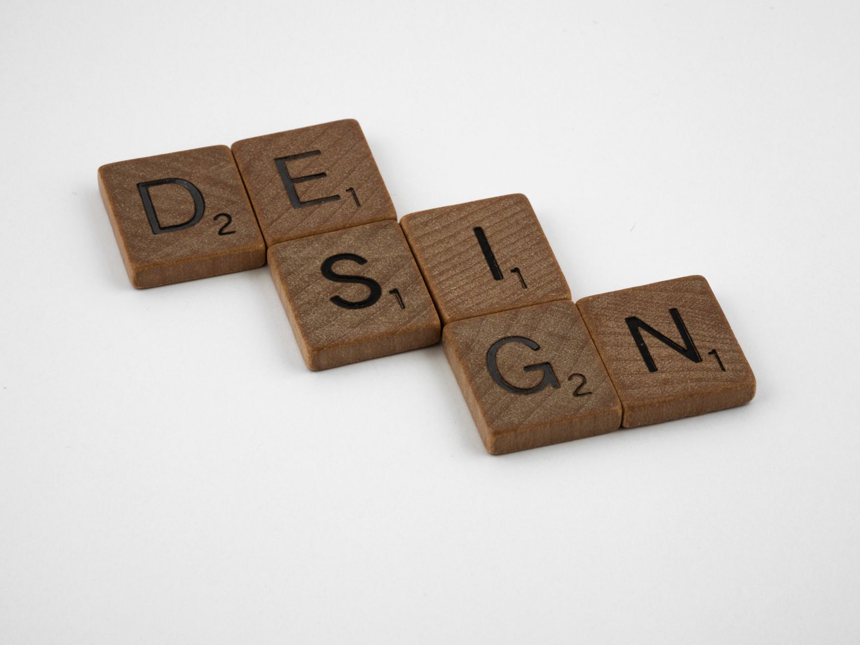 Close-up of wooden Scrabble tiles spelling 'Design' on a white background.