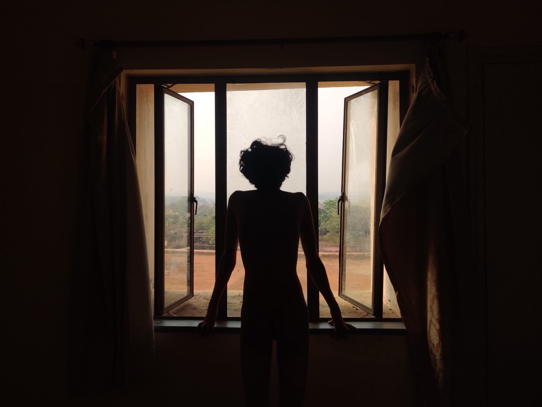 Silhouette of a woman standing at an open window in Jatni, India during daytime.