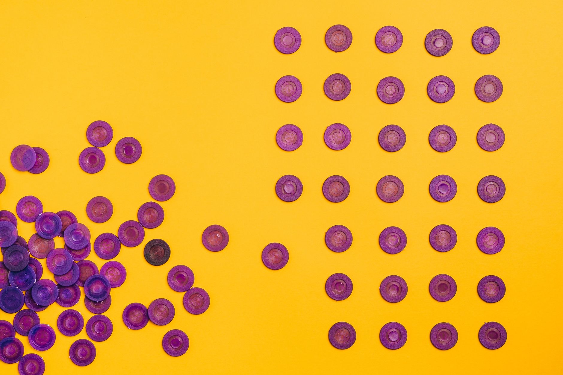 Arrangement of scattered and orderly purple discs on a vibrant yellow background creates a striking contrast.