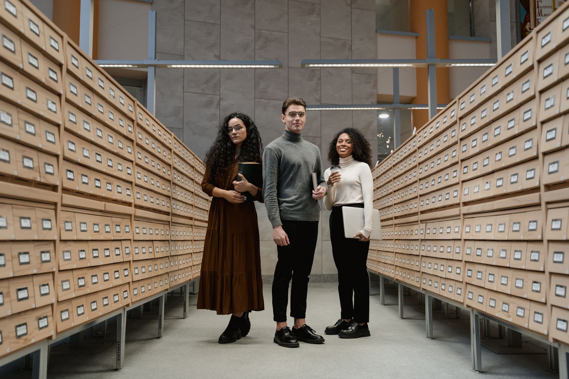 Three students stand in a library archive, symbolizing diversity and learning.