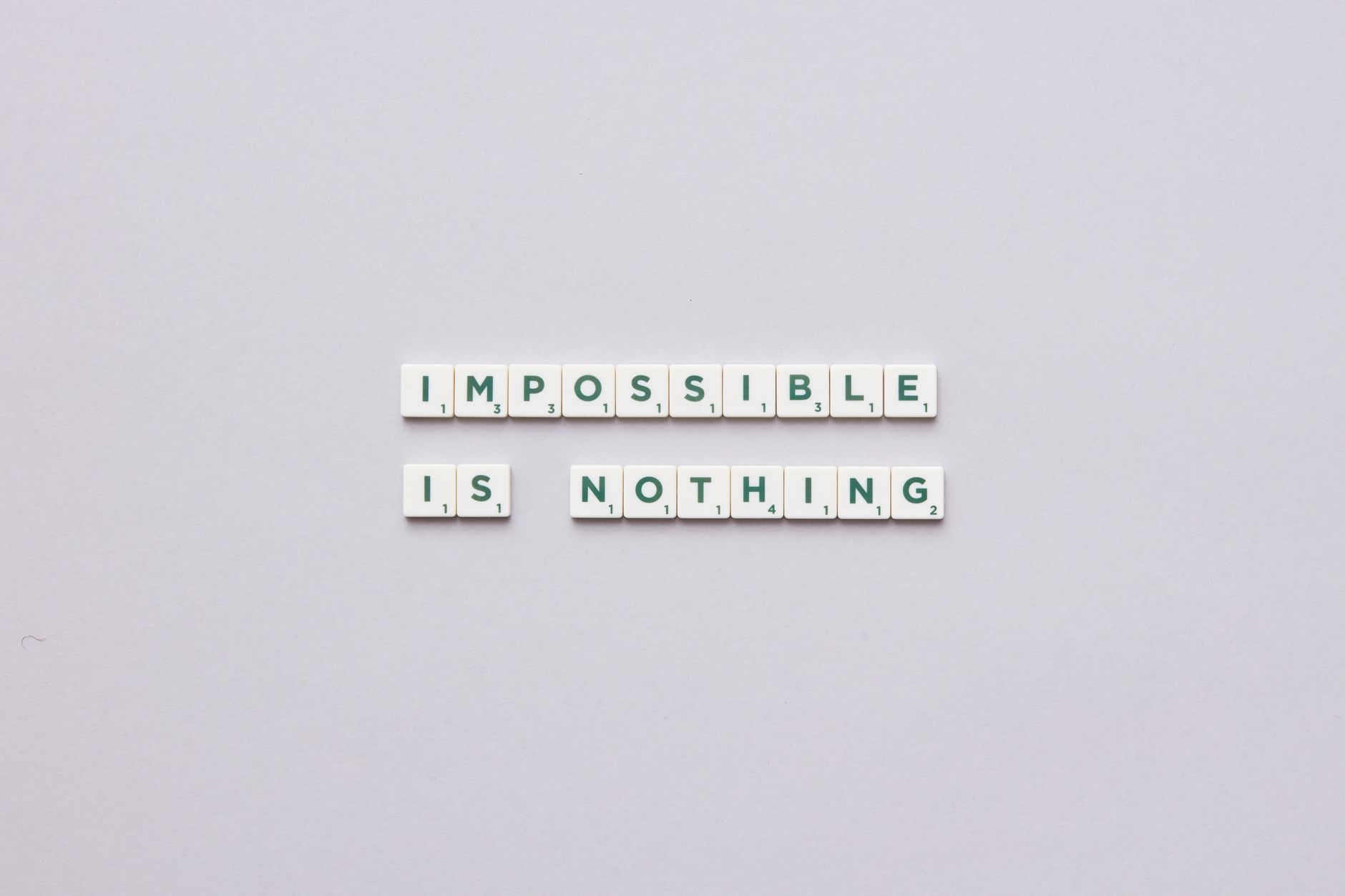 Flat lay of Scrabble tiles spelling 'Impossible is Nothing' on a neutral background.