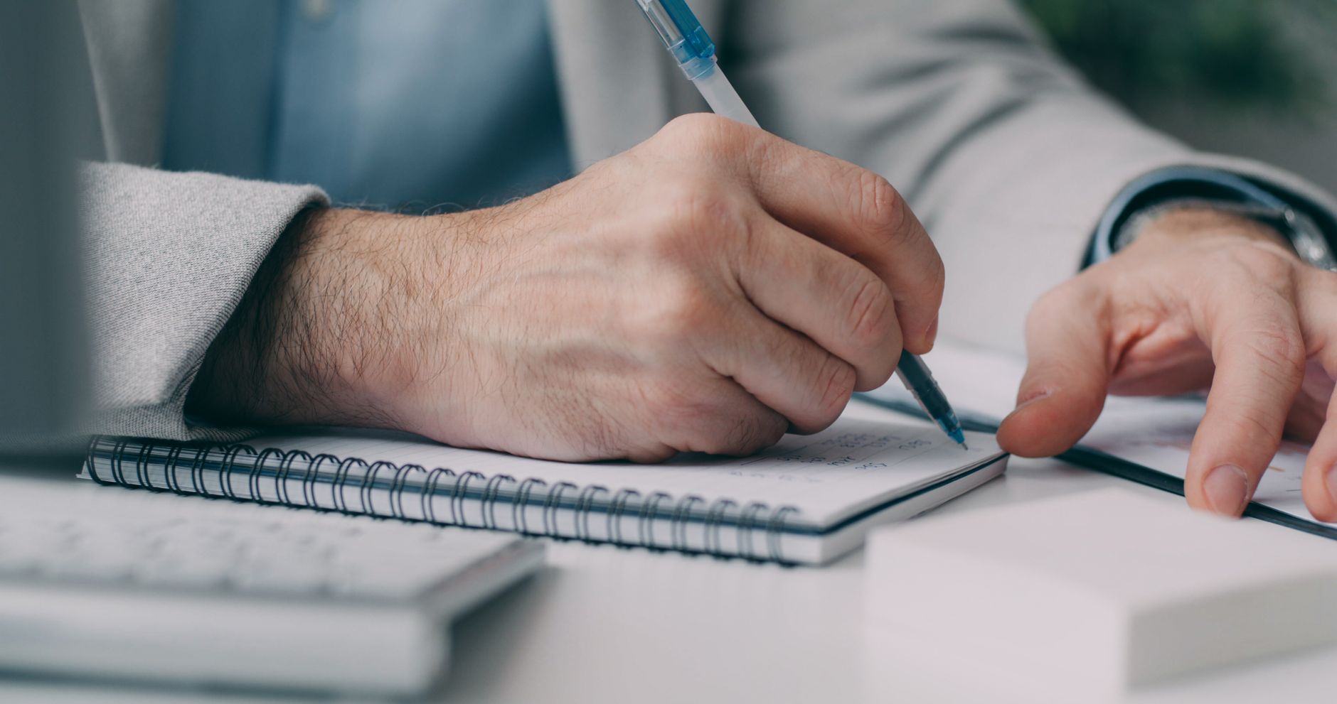 Close-up of a businessman taking notes in a notebook at a desk.
