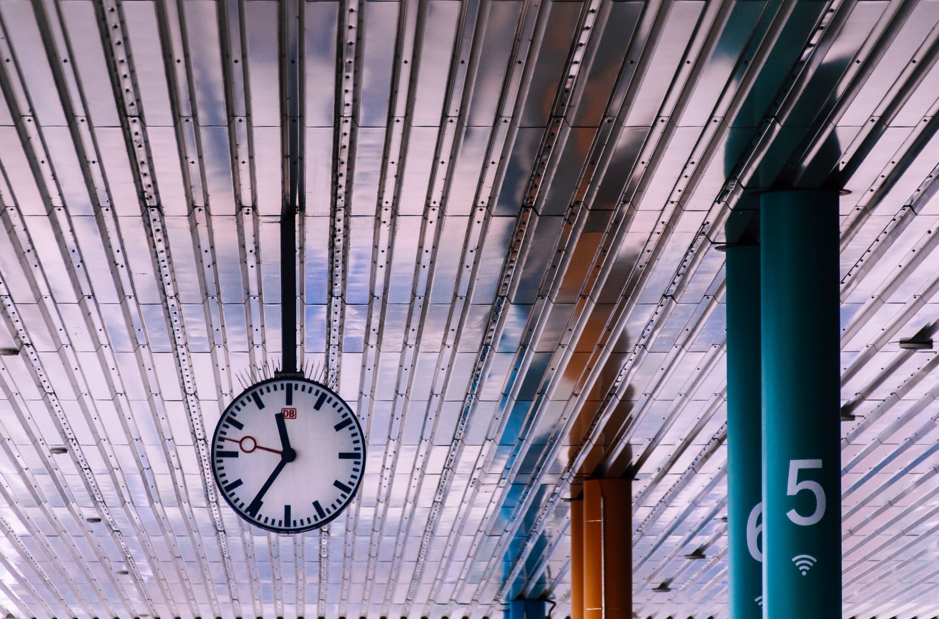 View of a modern train station ceiling with metal panels and a large clock.