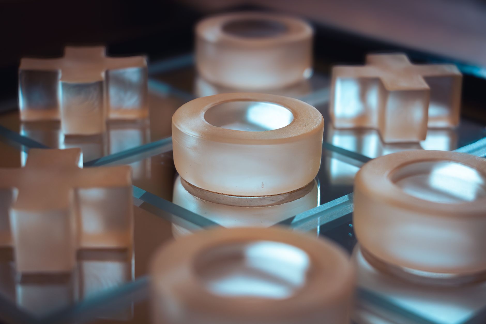 Close-up of a modern glass tic-tac-toe board with circular and cross pieces.