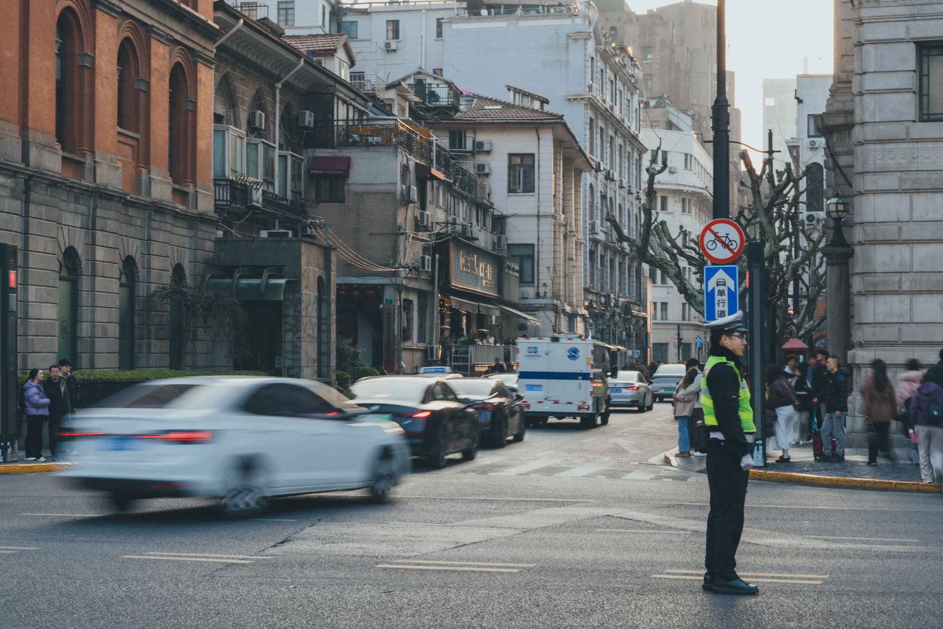 An urban street bustling with cars and people, featuring a traffic officer directing vehicles in a vibrant cityscape.