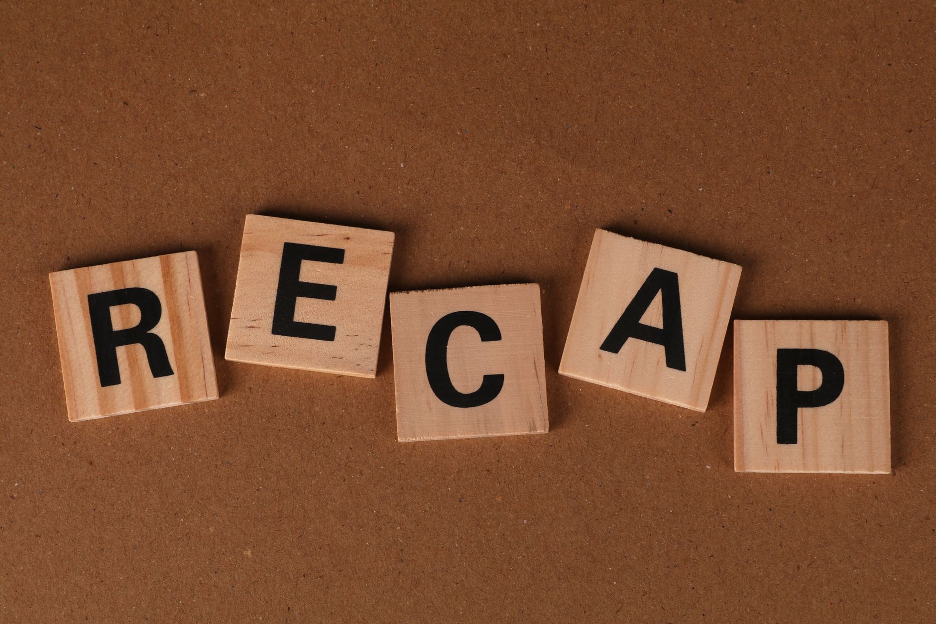 Wooden Scrabble tiles spelling 'RECAP' on a brown textured background. Text concept image.