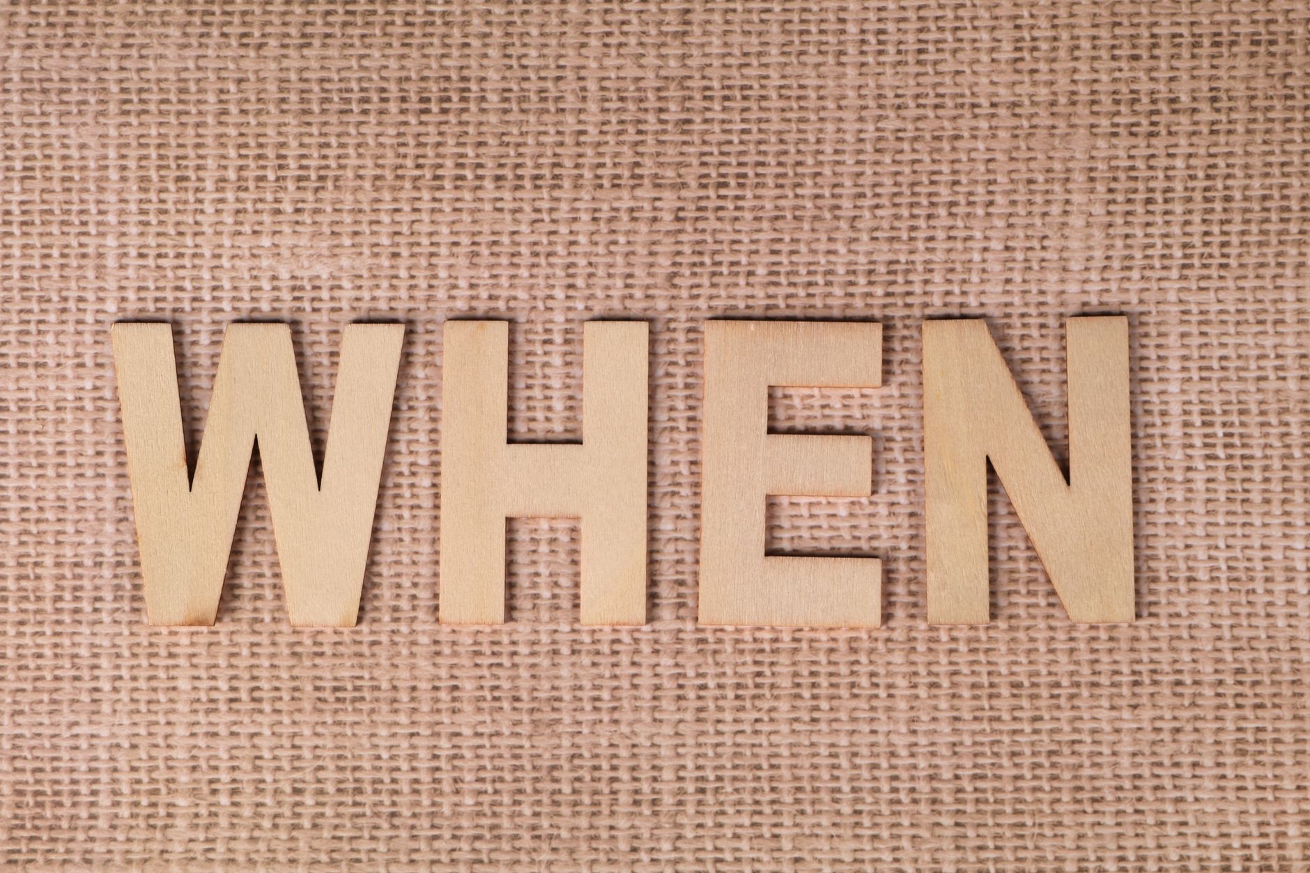Wooden letters spelling "WHEN" on a textured burlap surface, ideal for concepts of time and planning.