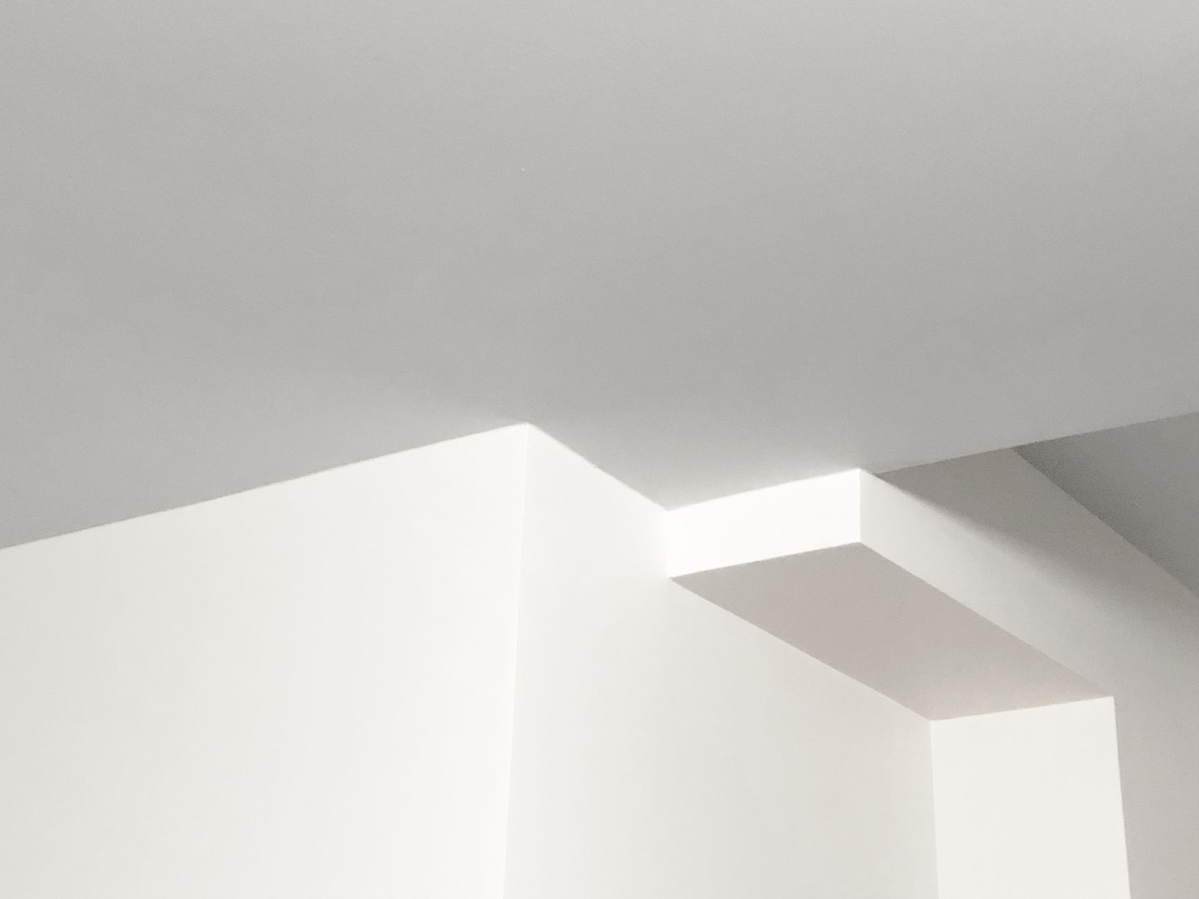 A minimalist design featuring a white ceiling with geometric structures creating soft shadows.