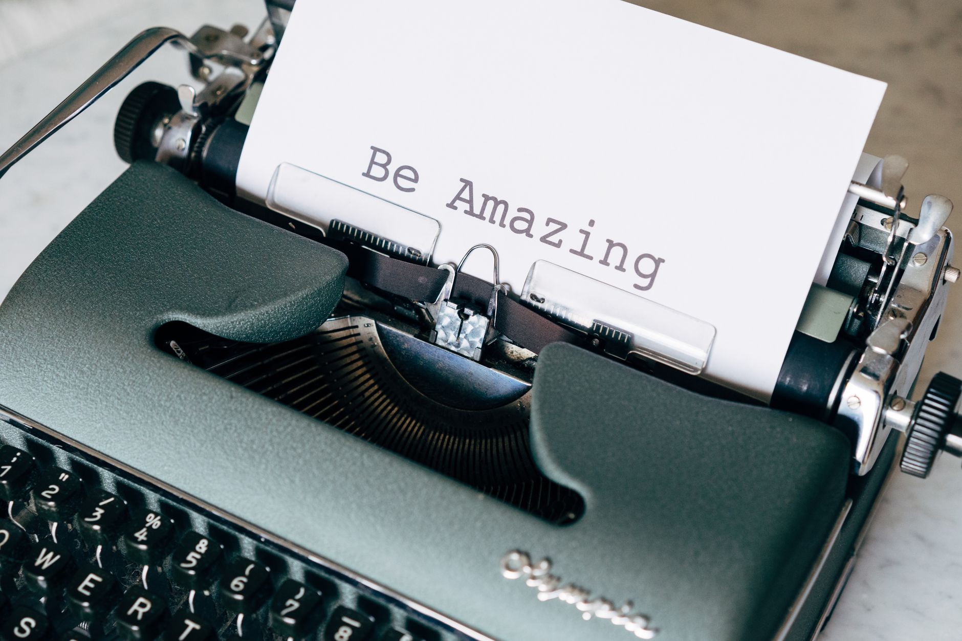 Close-up of a vintage typewriter typing 'Be Amazing' on white paper, conceptual style.