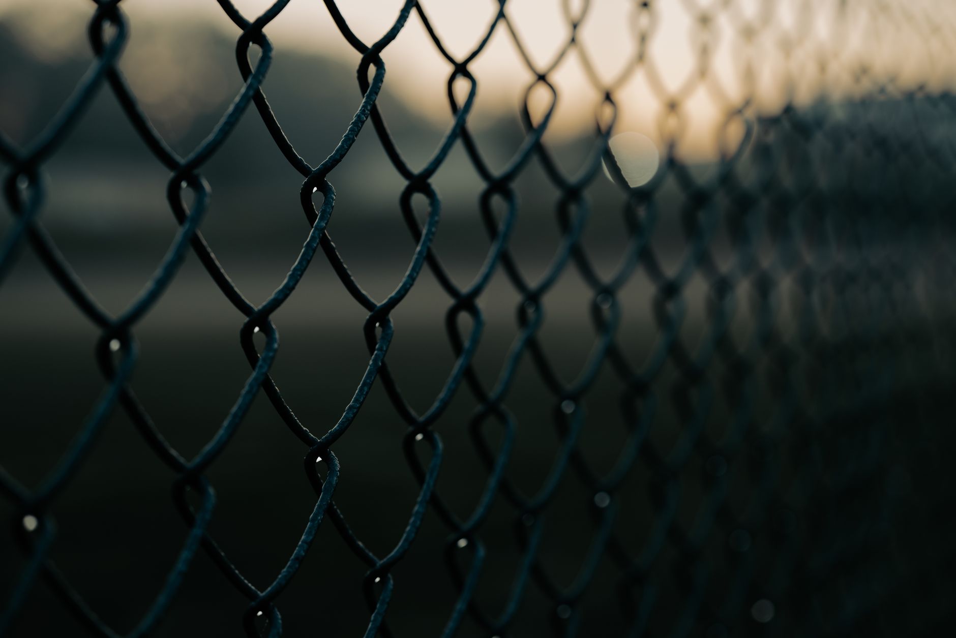 Close-up shot of a chain link fence with selective focus, creating a moody atmosphere.