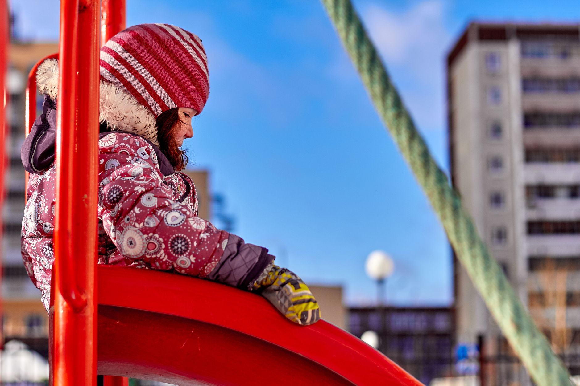 Cozy winter day with a child enjoying a playground slide. Bright attire and snowy backdrop.