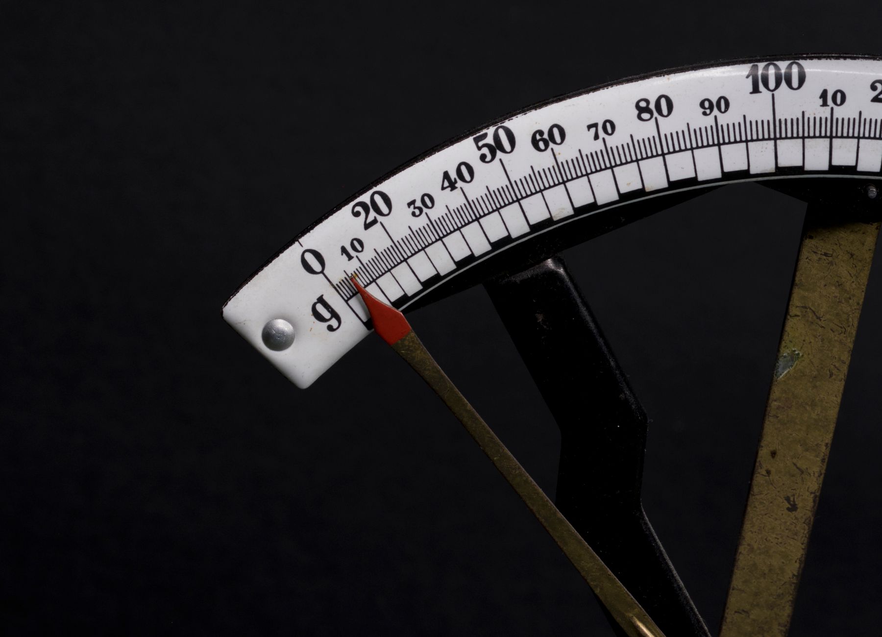 Detailed close-up image of a vintage analog weighing scale with a pointer against a black background.