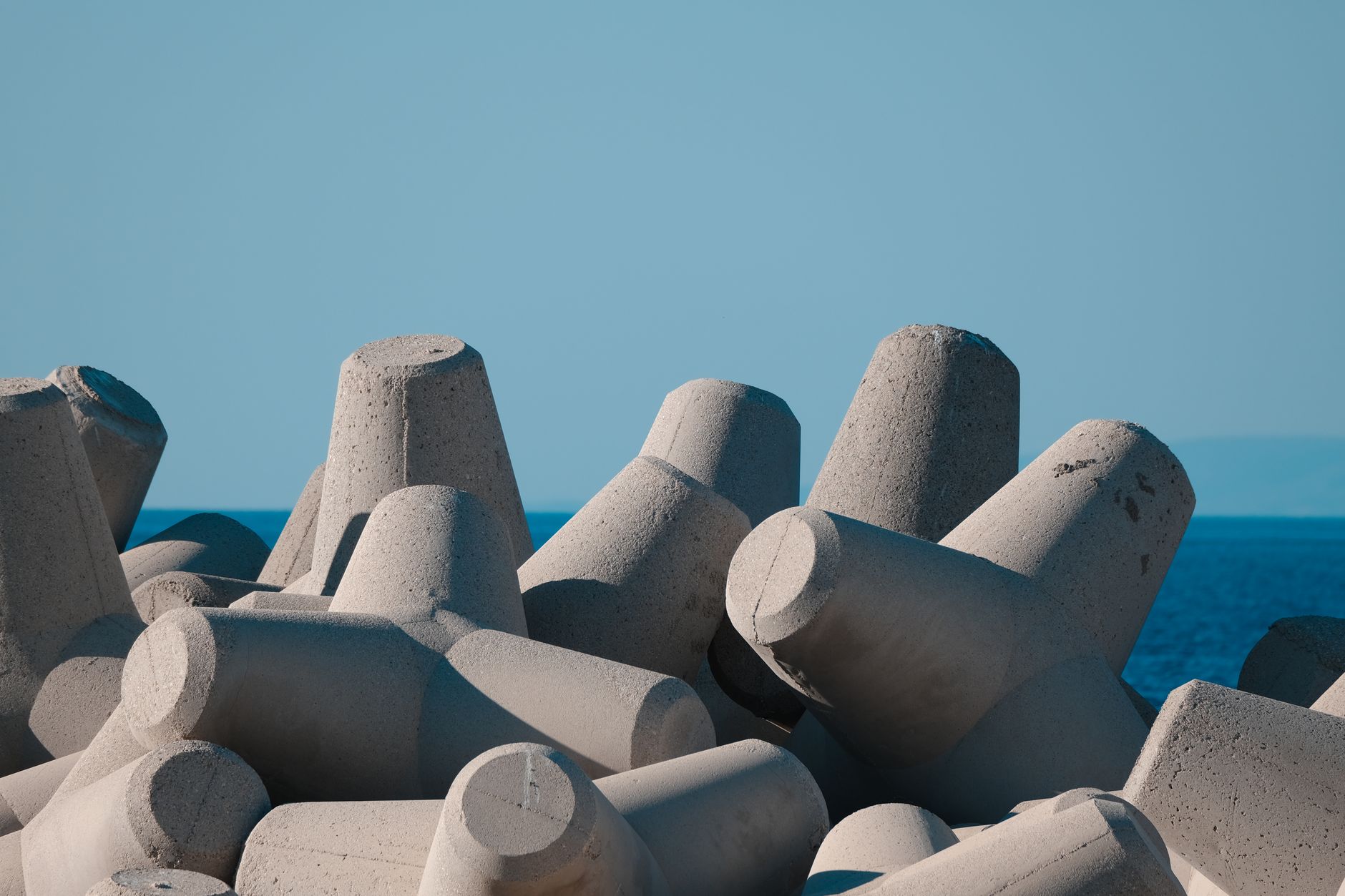 Photograph of concrete tetrapods on a seawall with a clear blue ocean backdrop under a sunny sky.