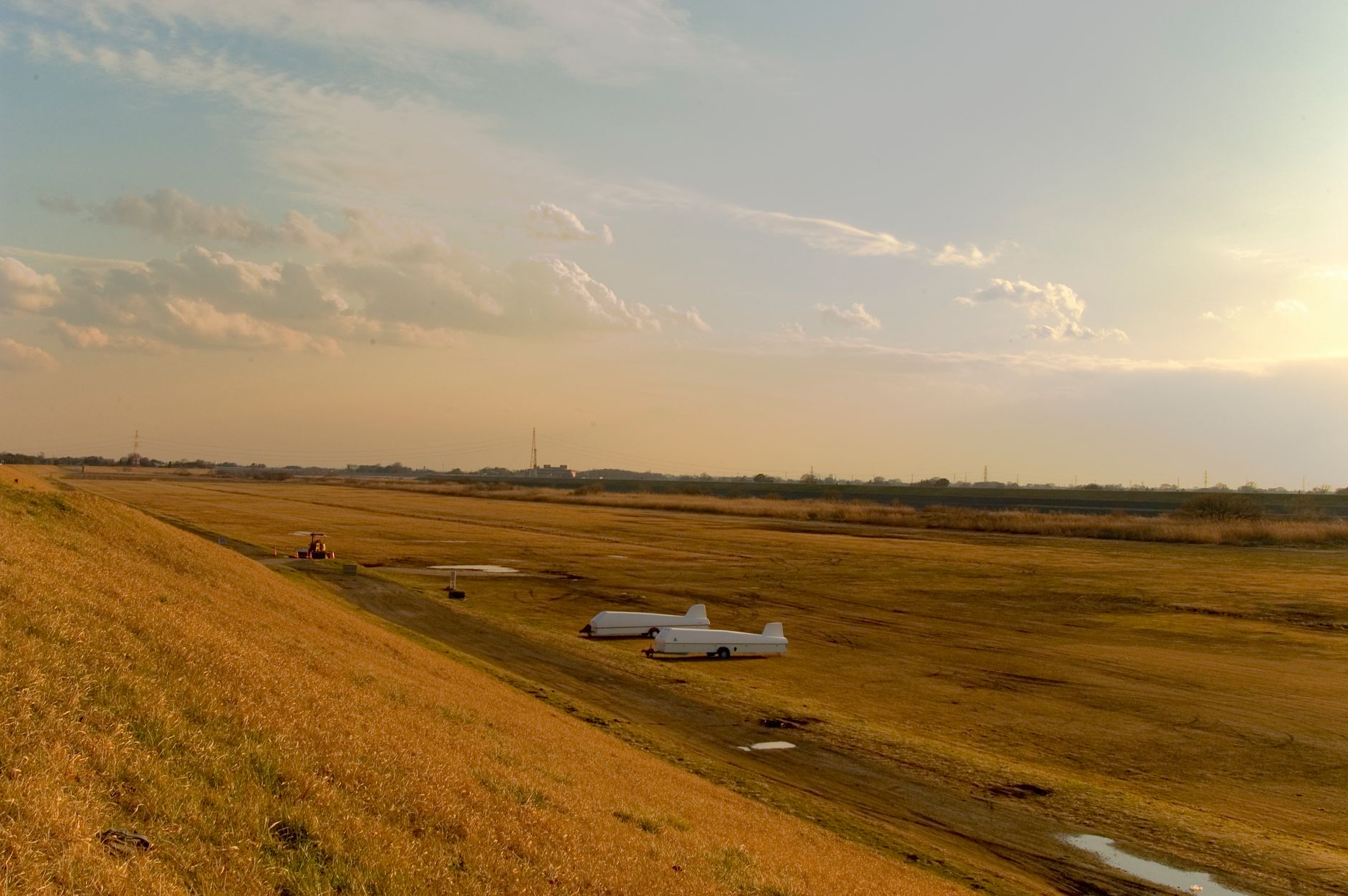 Serene countryside airfield with gliders parked on a grassy field under a warm sunset sky.