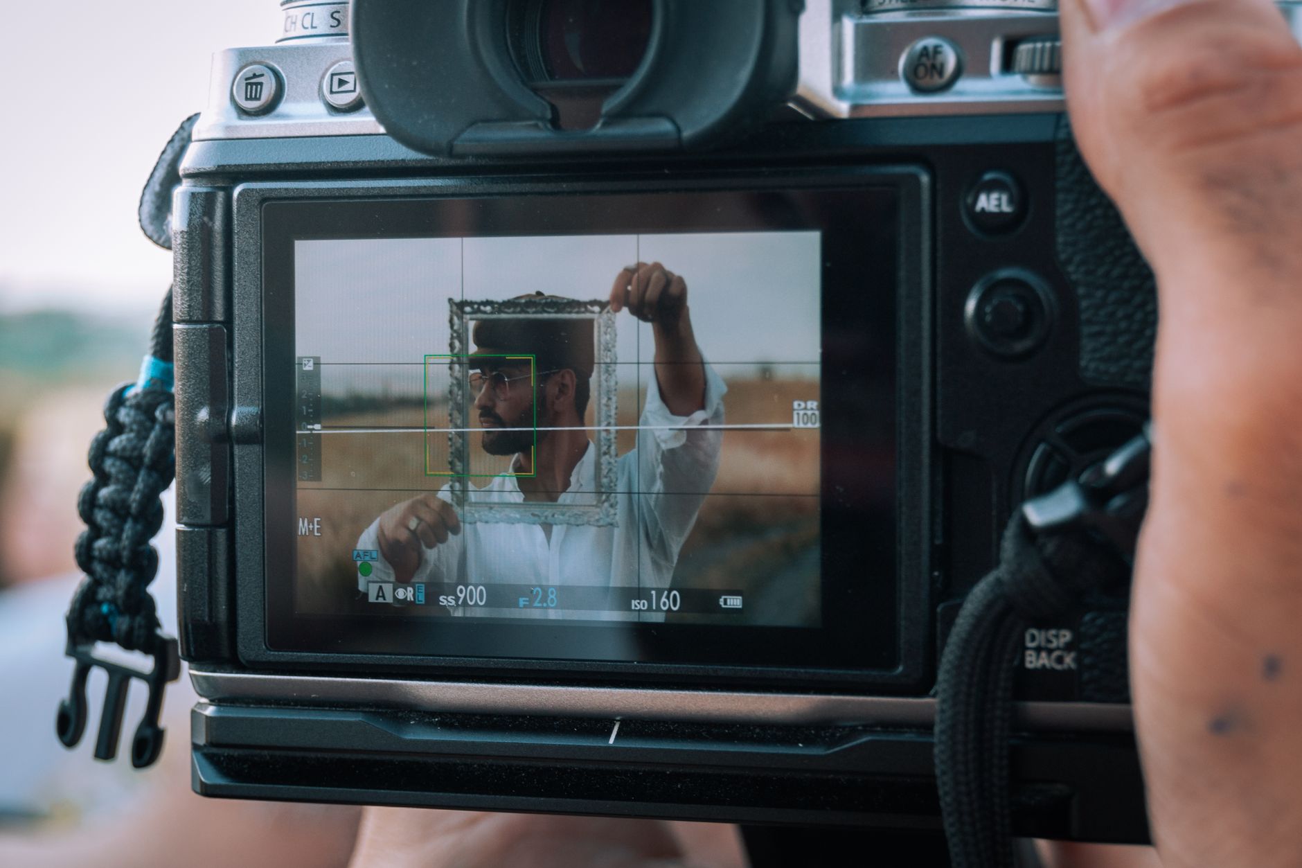 A man holding a mirror is visible through a digital camera's viewfinder, showcasing photography techniques.