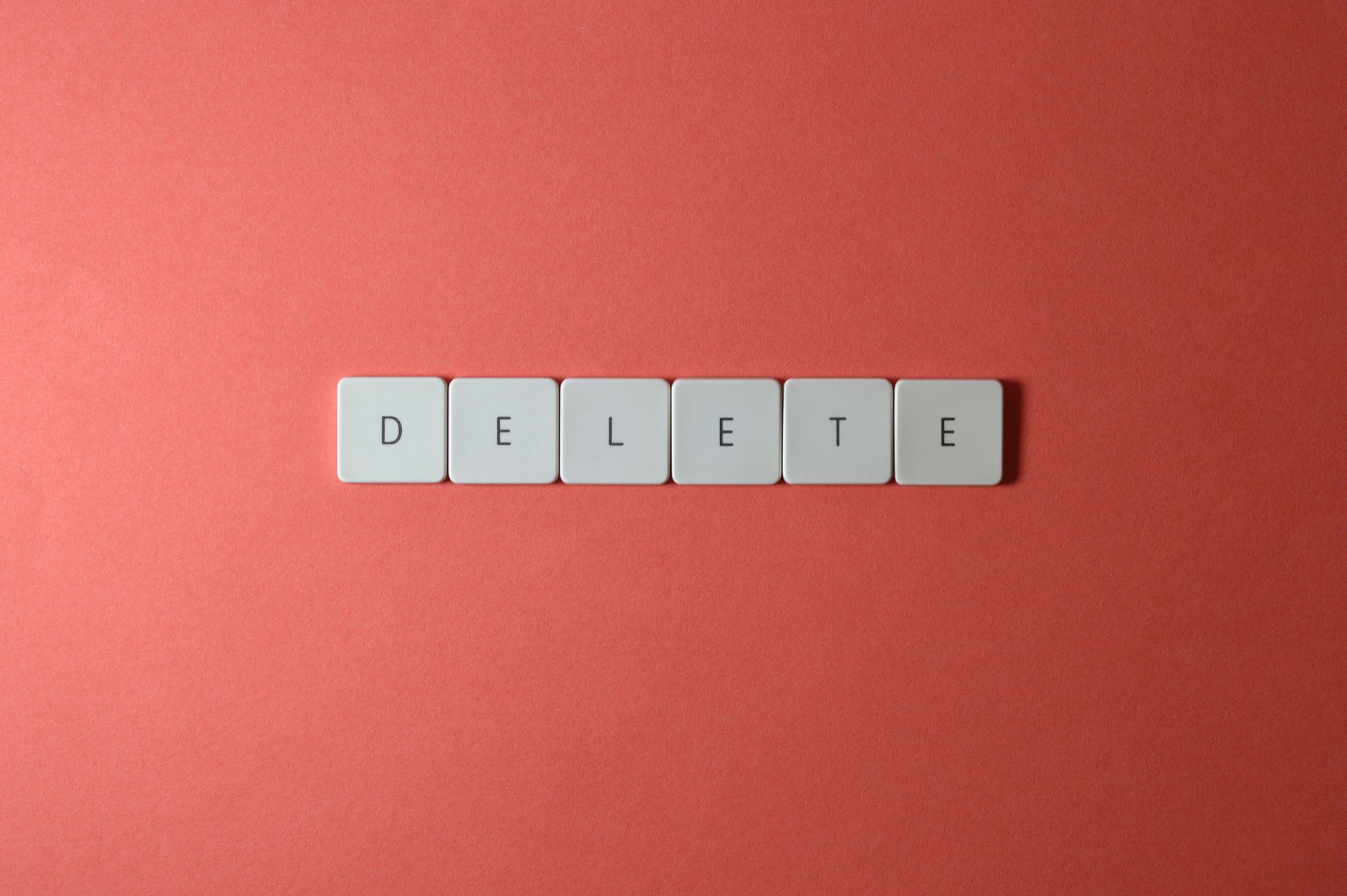 Close-up of keyboard letters spelling 'DELETE' on a coral background, emphasizing digital concepts.