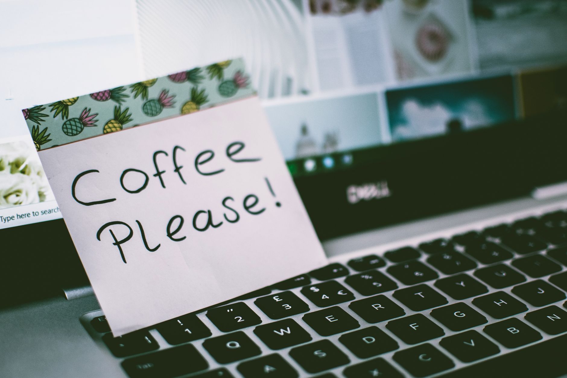 Close-up of a laptop keyboard with a note reading 'Coffee Please!' placed on top, suggesting a coffee break.