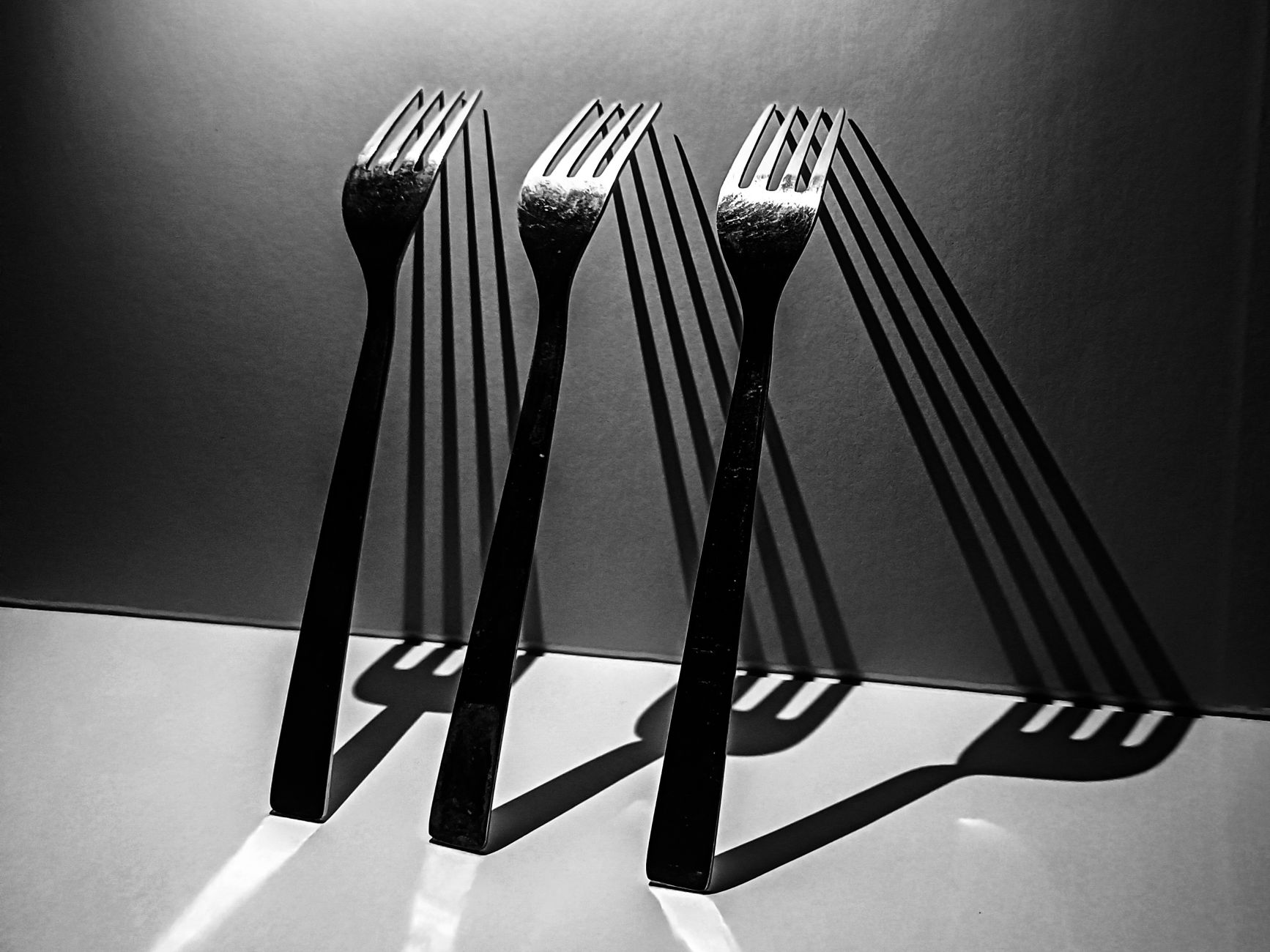 Three forks casting dramatic shadows against a minimalist backdrop in black and white.