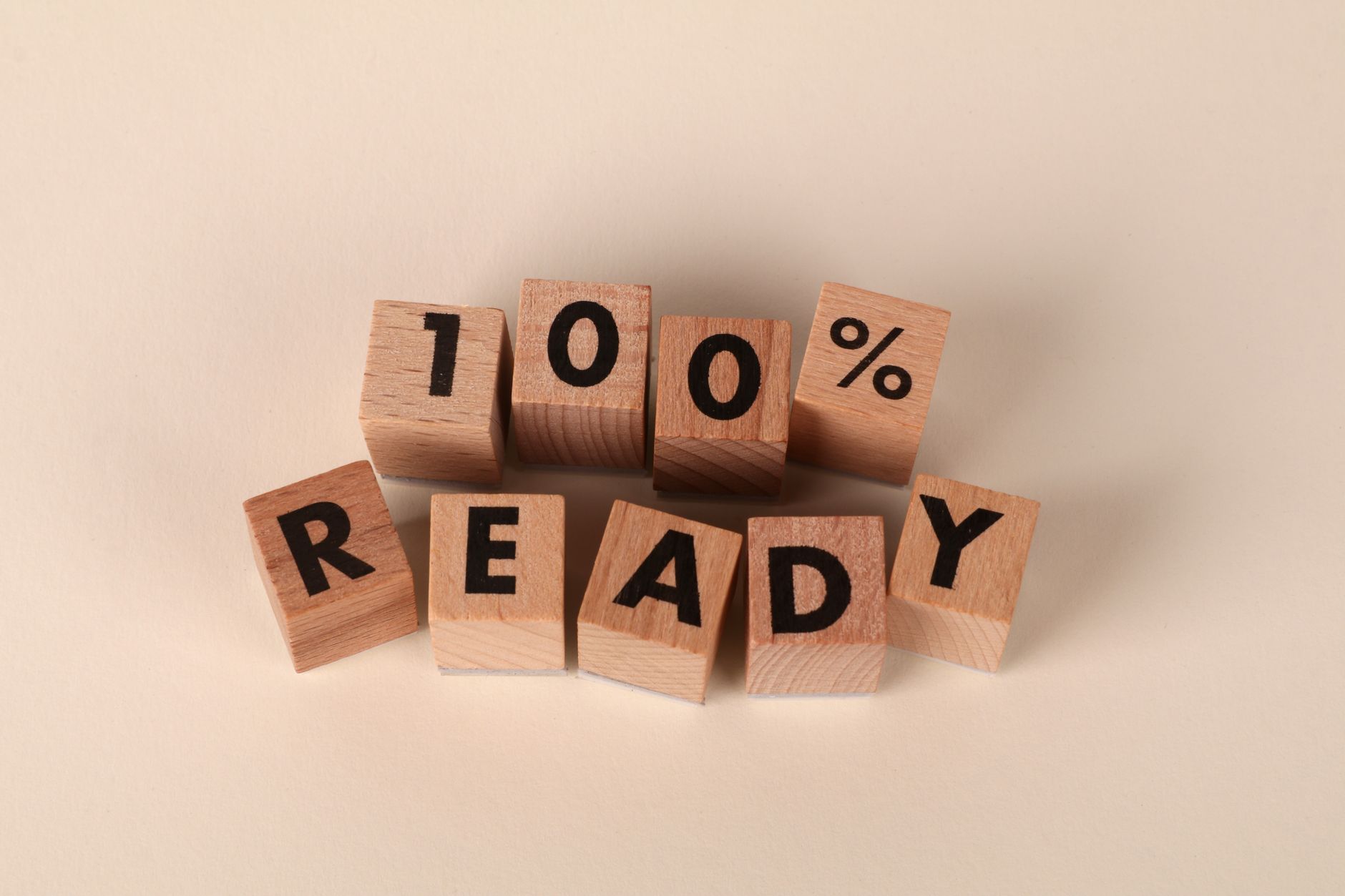 Wooden blocks arranged to show the text '100% Ready' on a neutral background, symbolizing preparedness and confidence.