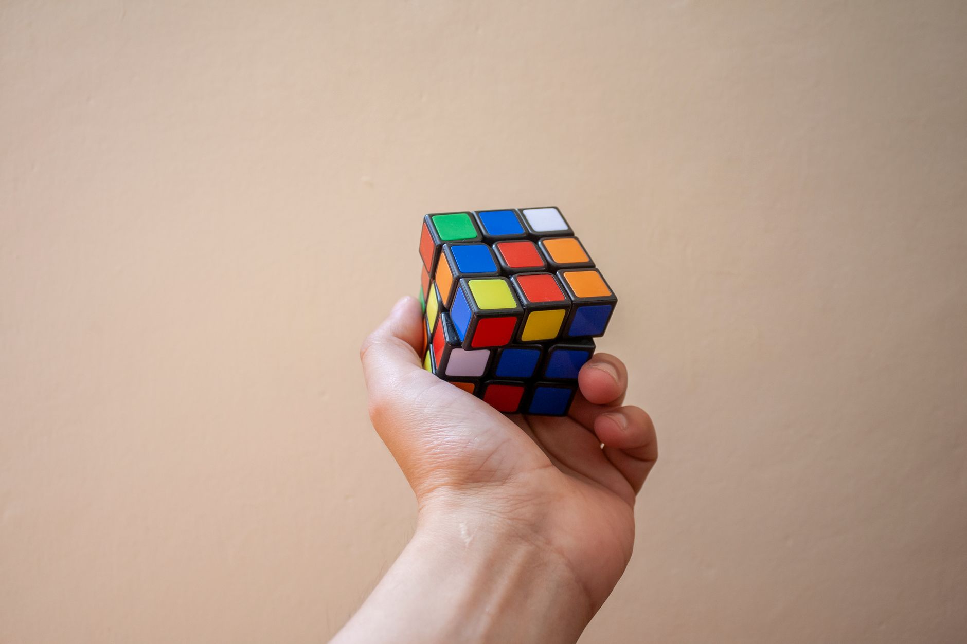 Close-up of a hand holding a colorful Rubik's Cube against a neutral background.