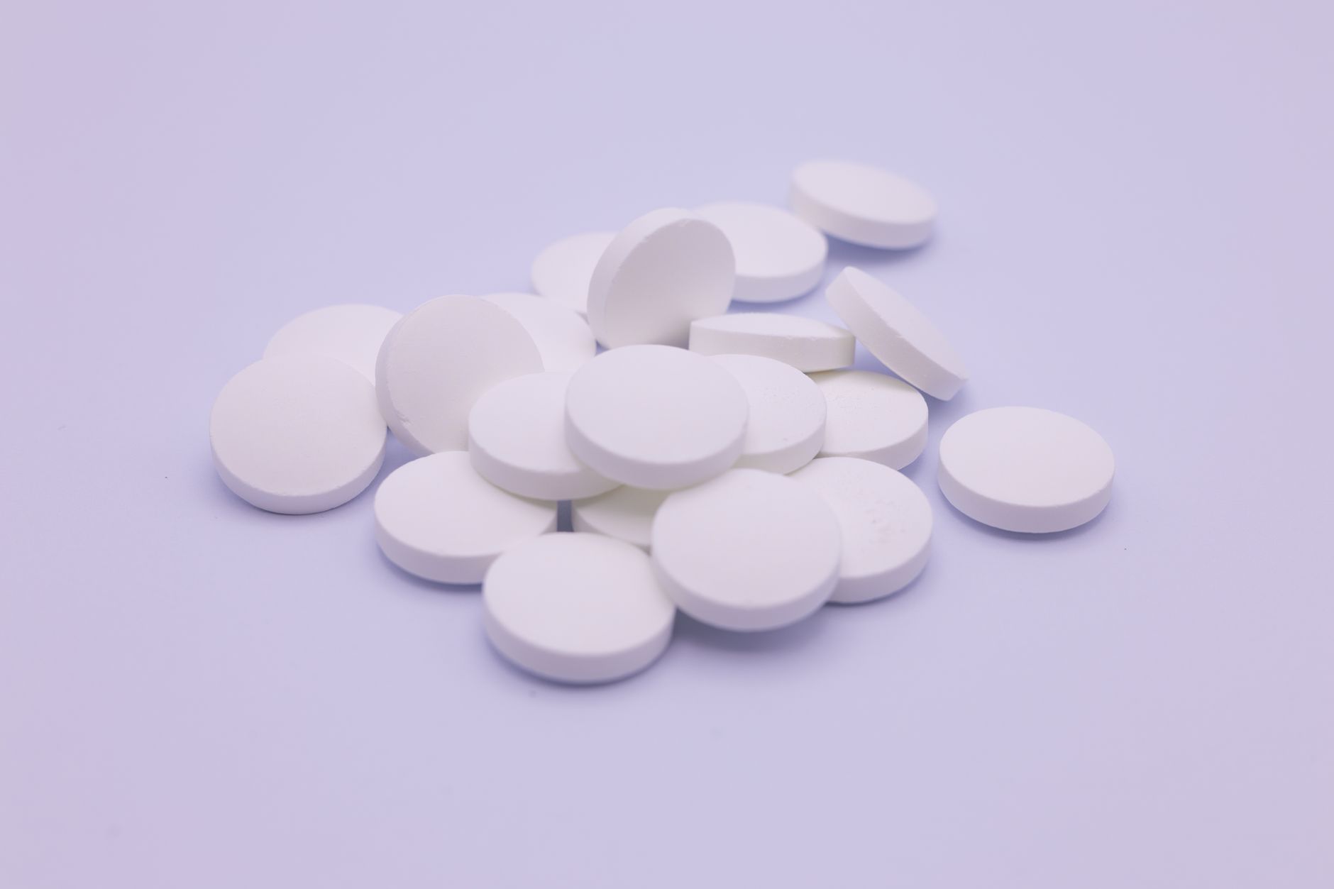 Assorted white tablets stacked on a soft purple surface, symbolizing medication and healthcare.