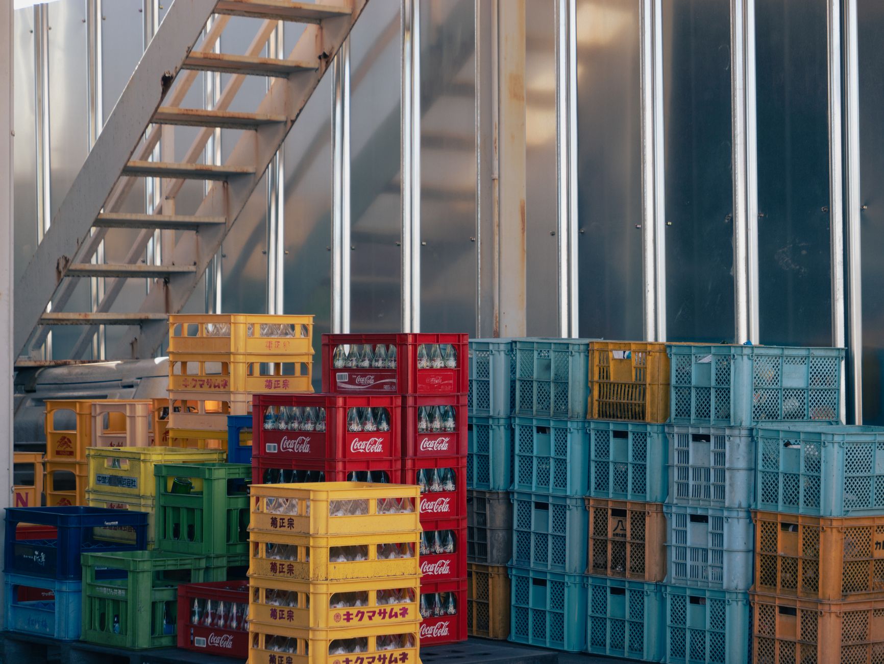 A collection of colorful crates stacked beside an industrial staircase outdoors.