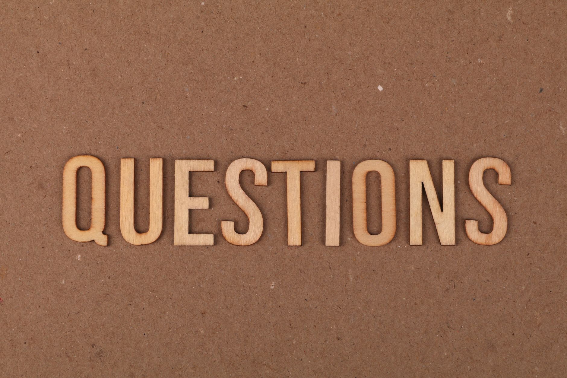 Wooden letters spelling the word "QUESTIONS" on a cardboard background, providing a neutral copyspace.