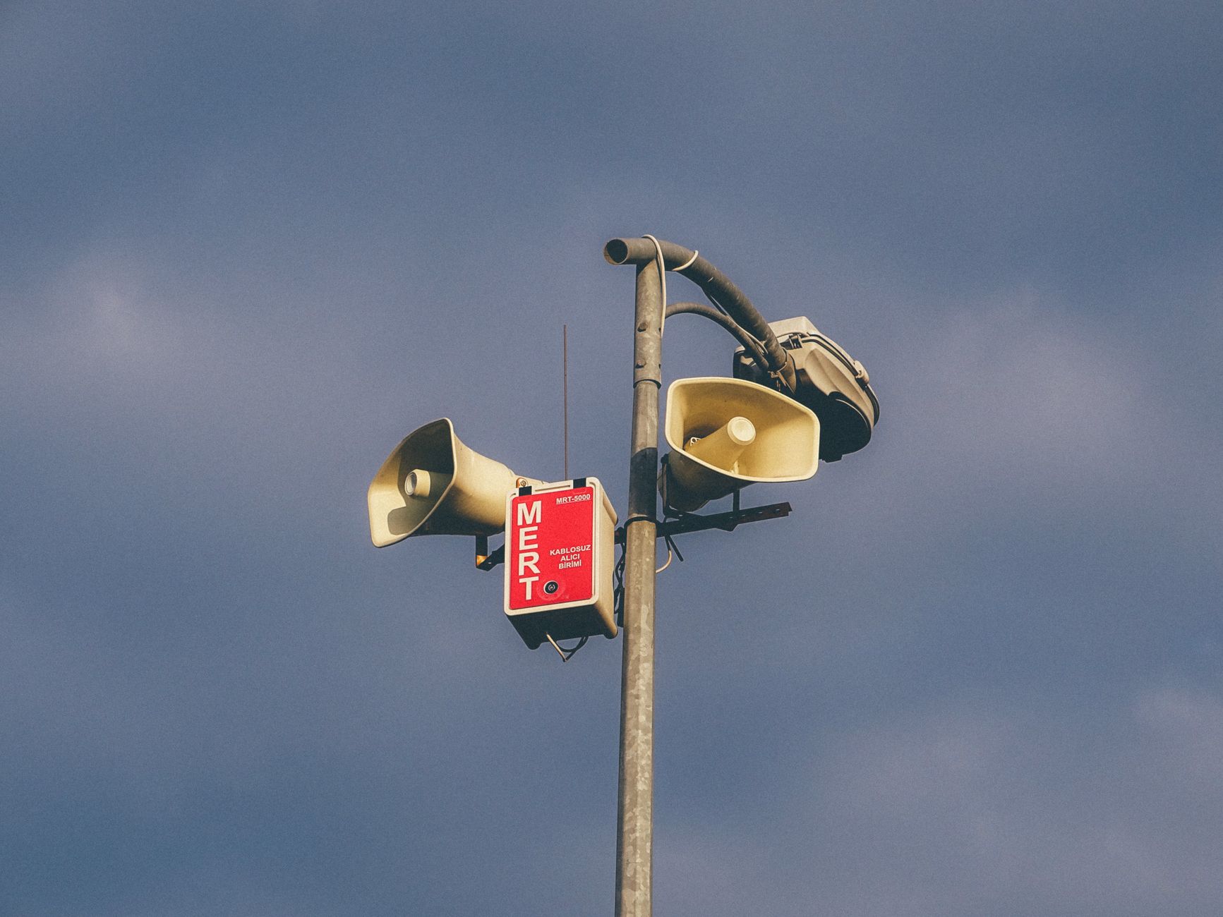 A warning system with loudspeakers on a pole against a cloudy sky, signaling emergency alerts.
