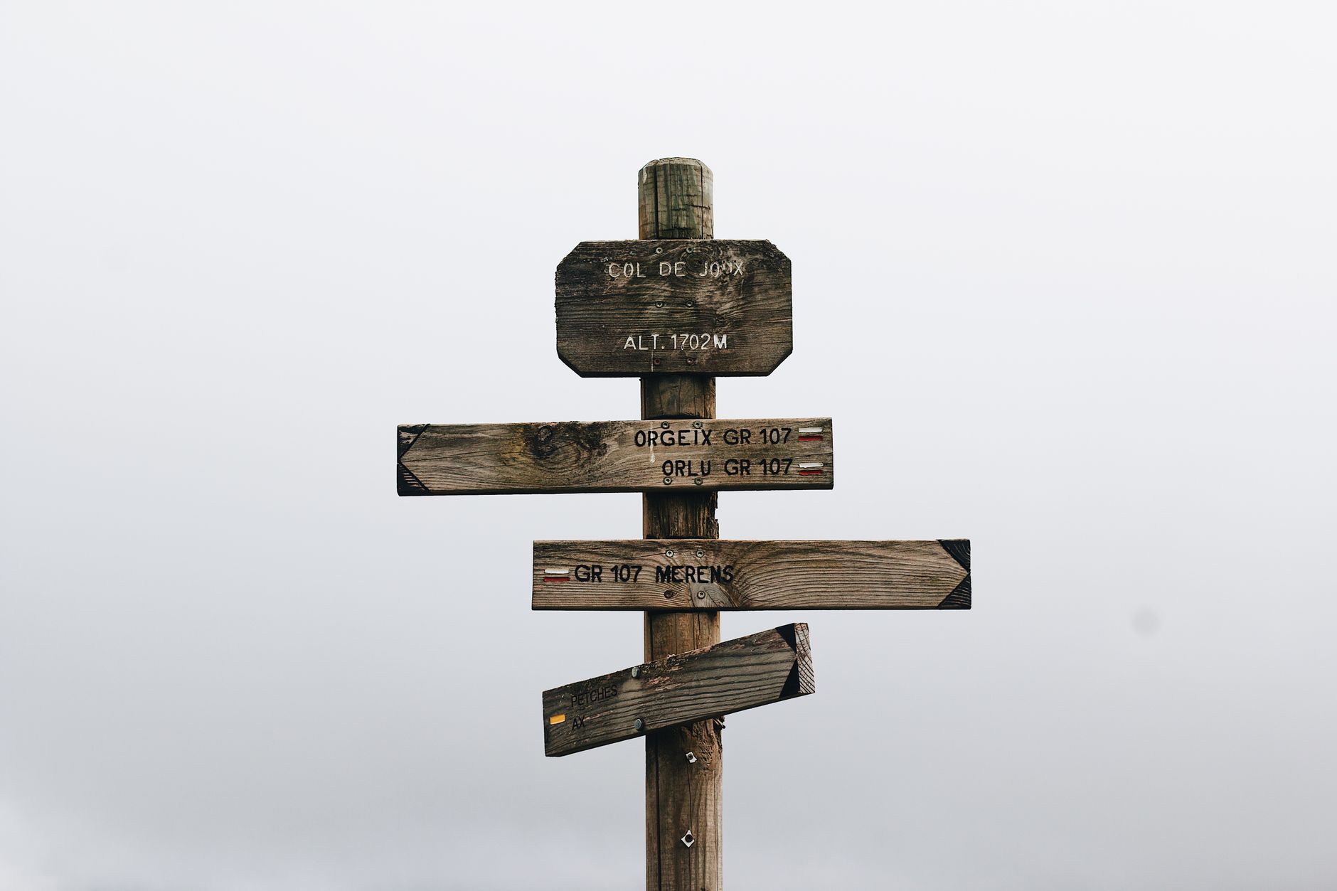 Vintage wooden signpost in foggy mountain landscape, indicating hiking trails and altitudes.