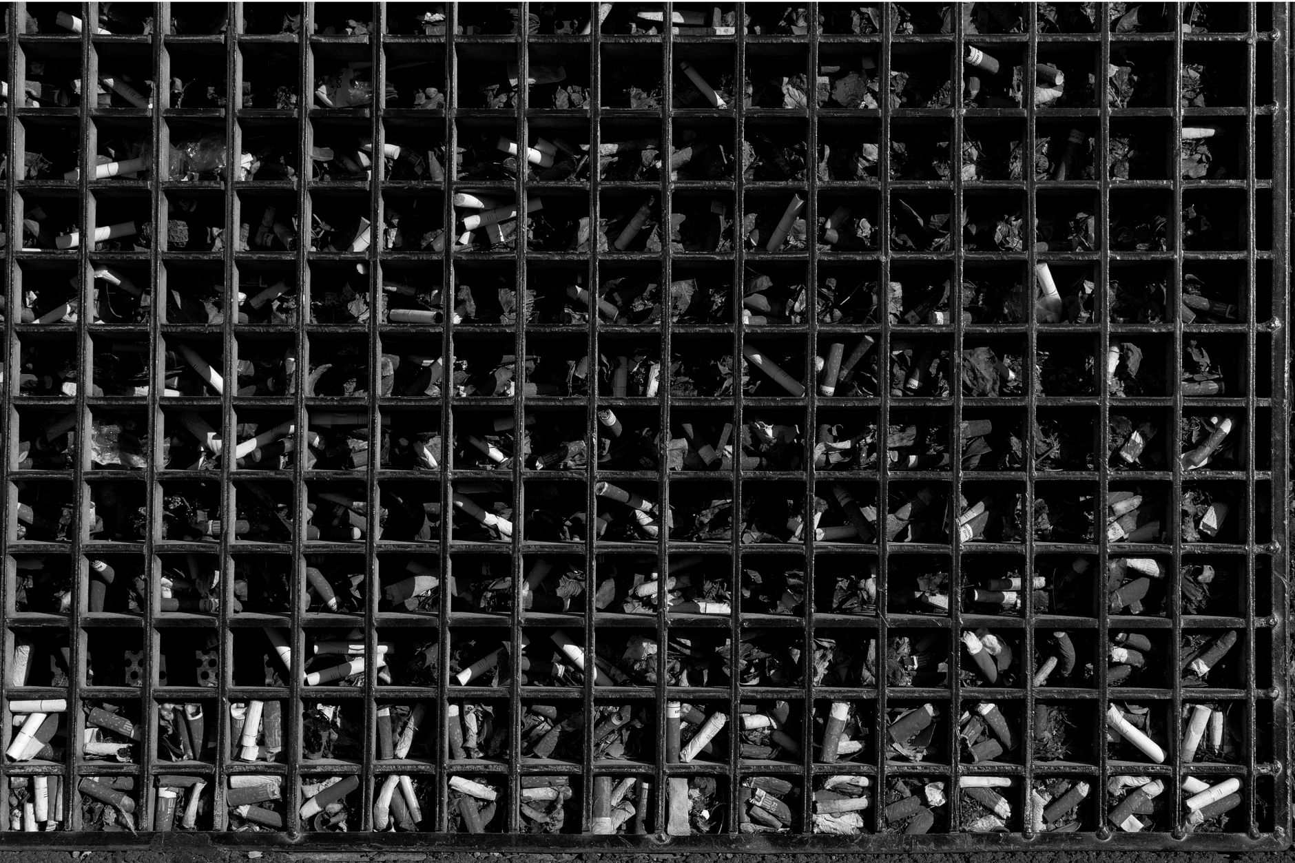 Close-up of cigarette butts trapped in a grid, illustrating pollution.