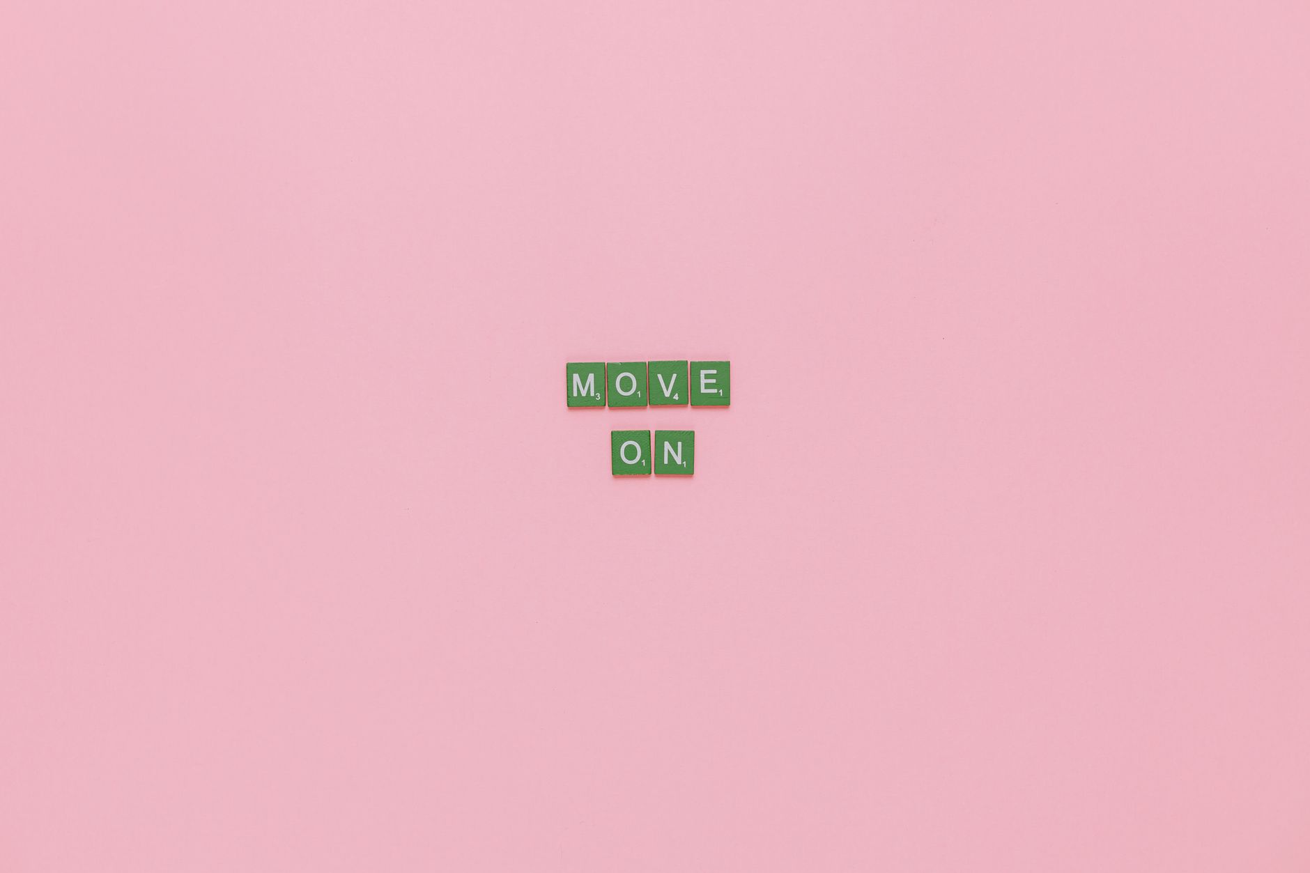 Inspirational text "Move On" spelled with green tiles on a pink background. Minimalist design, perfect for motivation.
