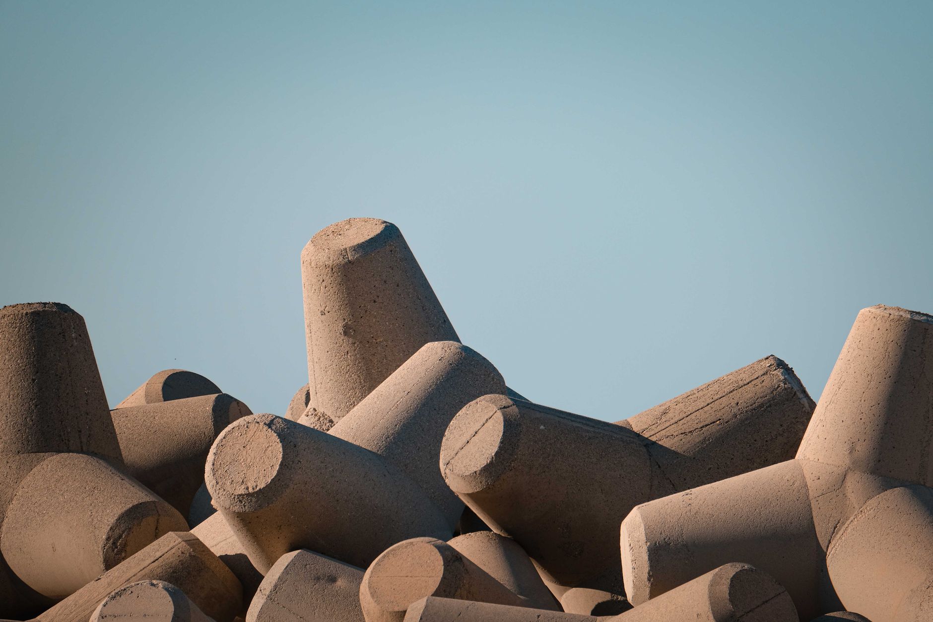 A pile of stacked concrete breakwater tetrapods under a clear blue sky, showcasing structural stability.