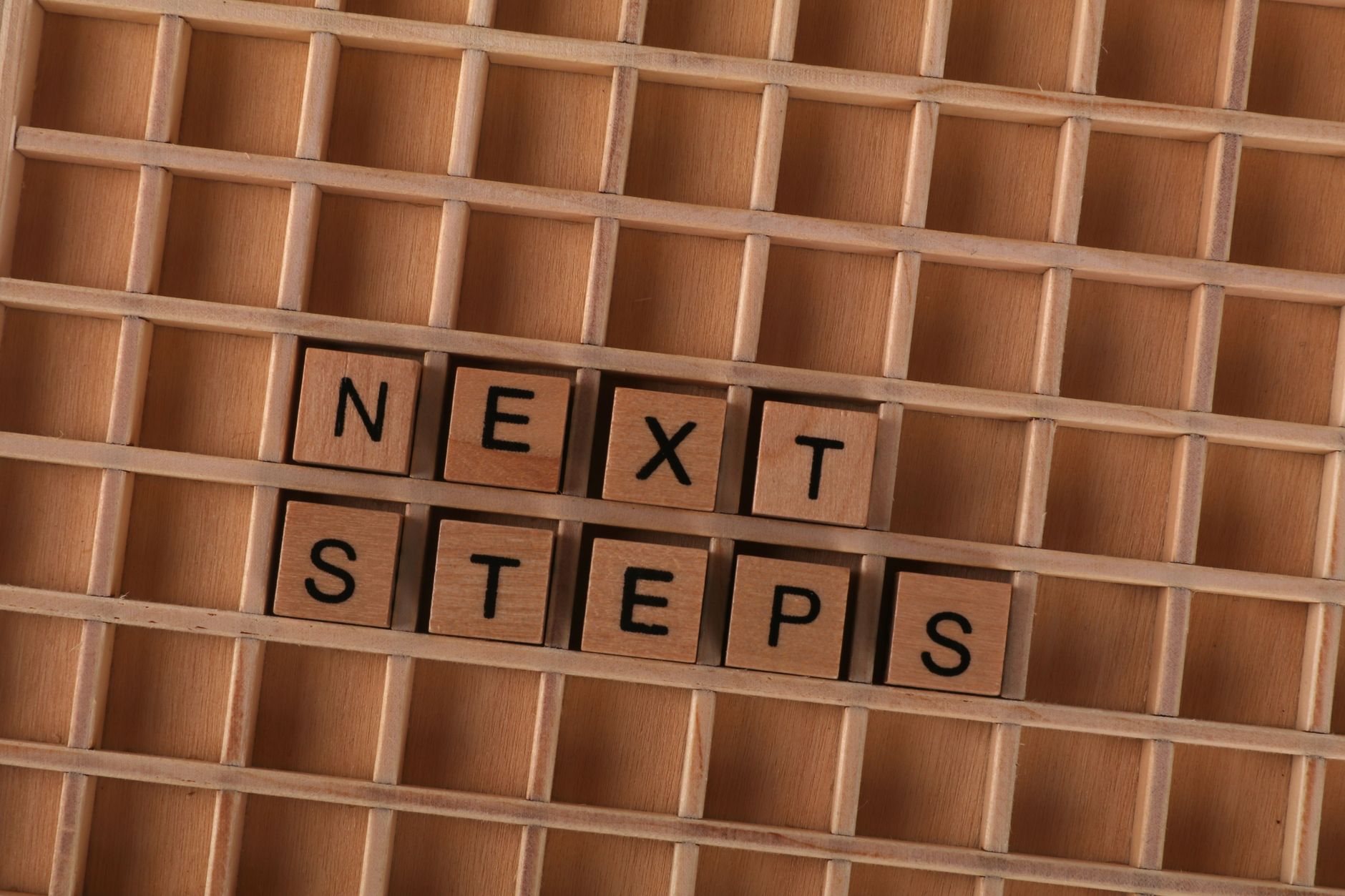 Flat lay of wooden letter blocks spelling 'Next Steps', inspiring progress and motivation.