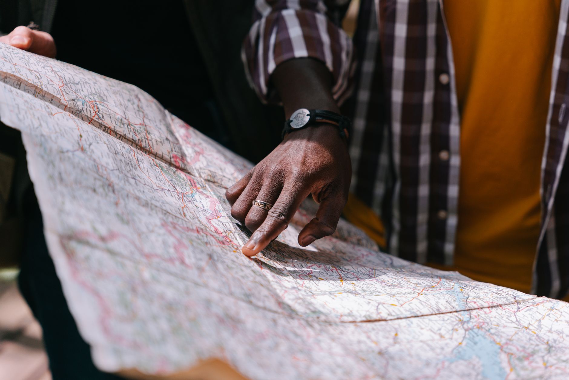 Close-up of a hand pointing at a detailed map, outdoors, wearing a striped shirt.