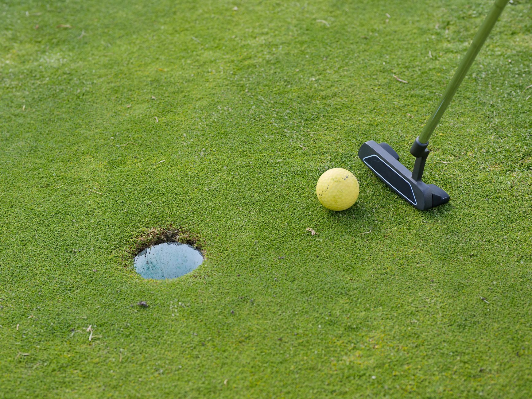 A golf ball and putter near a hole on a lush green golf course, ready for a putt.