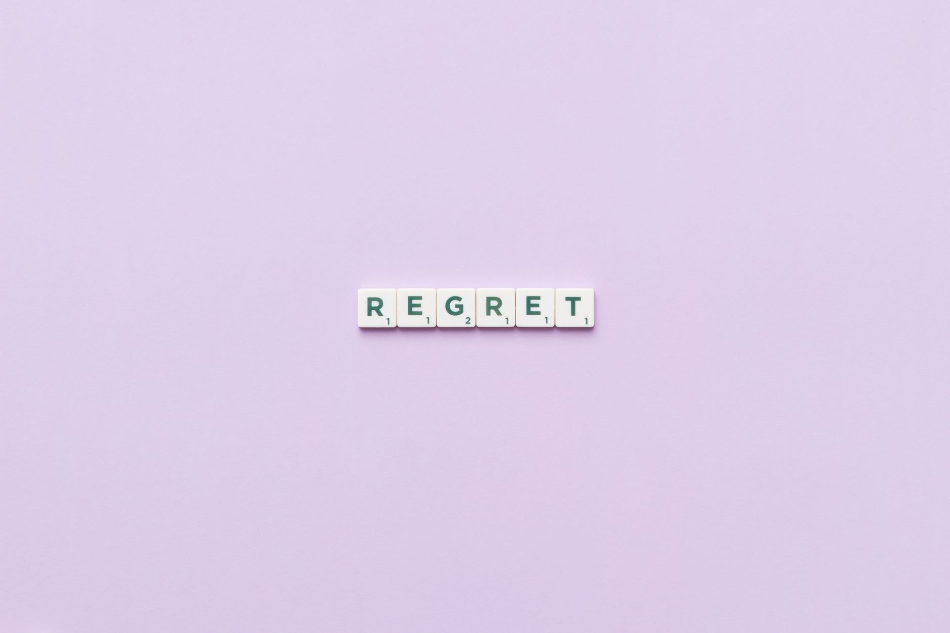 Scrabble tiles forming 'Regret' on a soft pink background, conveying a conceptual theme.