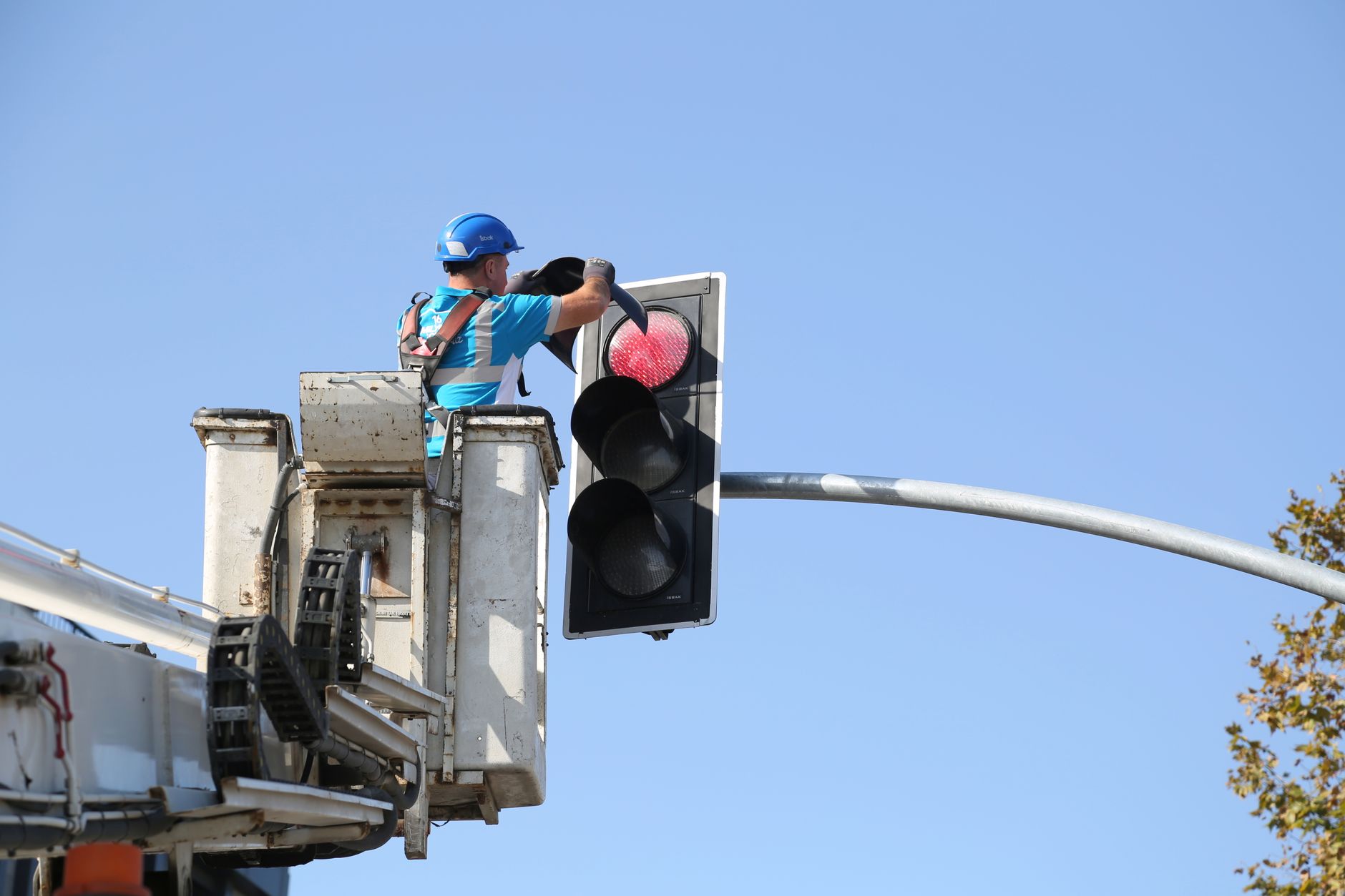 Man in safety gear adjusting traffic light on a clear day from lift.