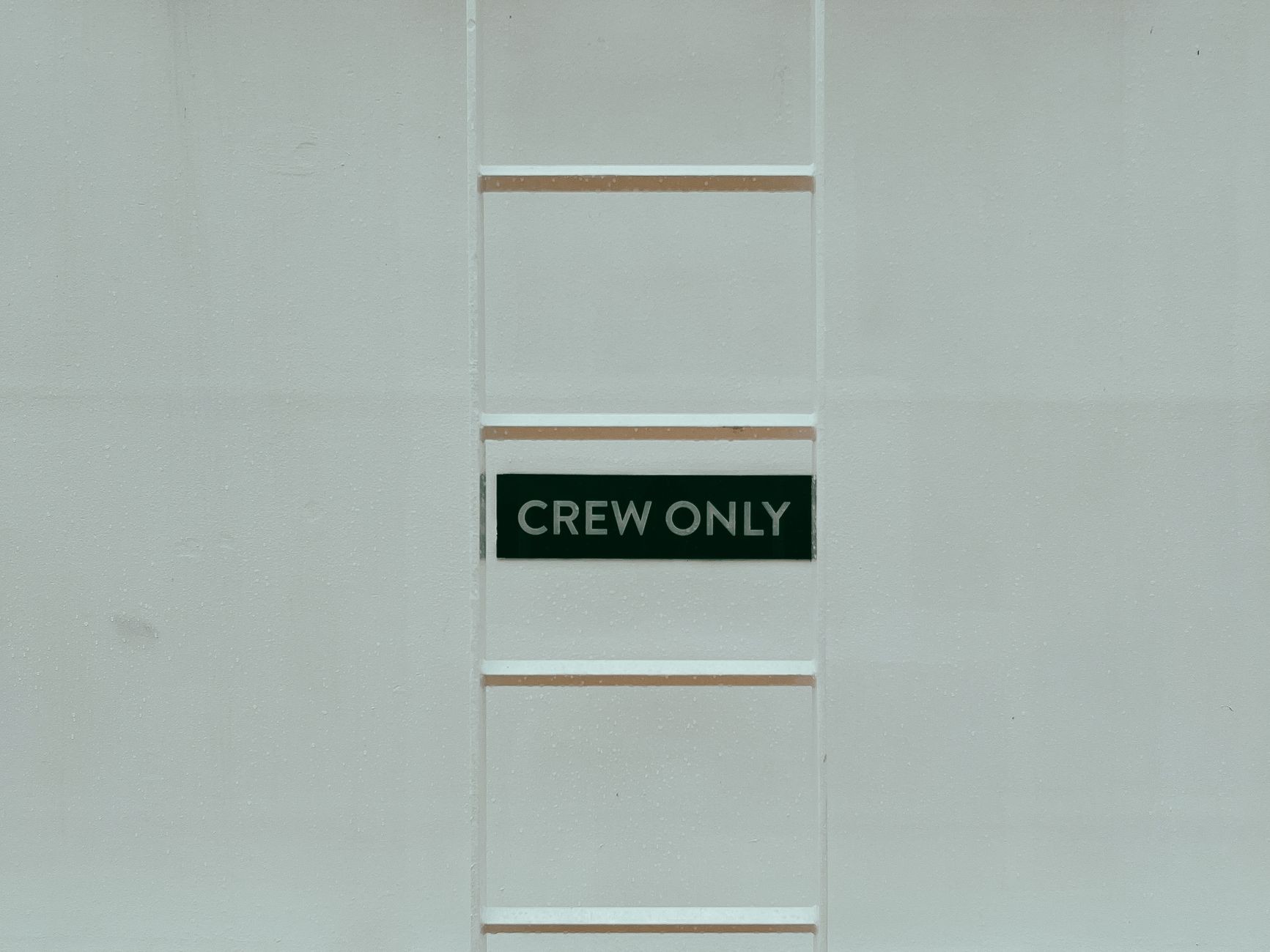 A minimalistic image featuring a 'Crew Only' sign on a ladder against a white wall.