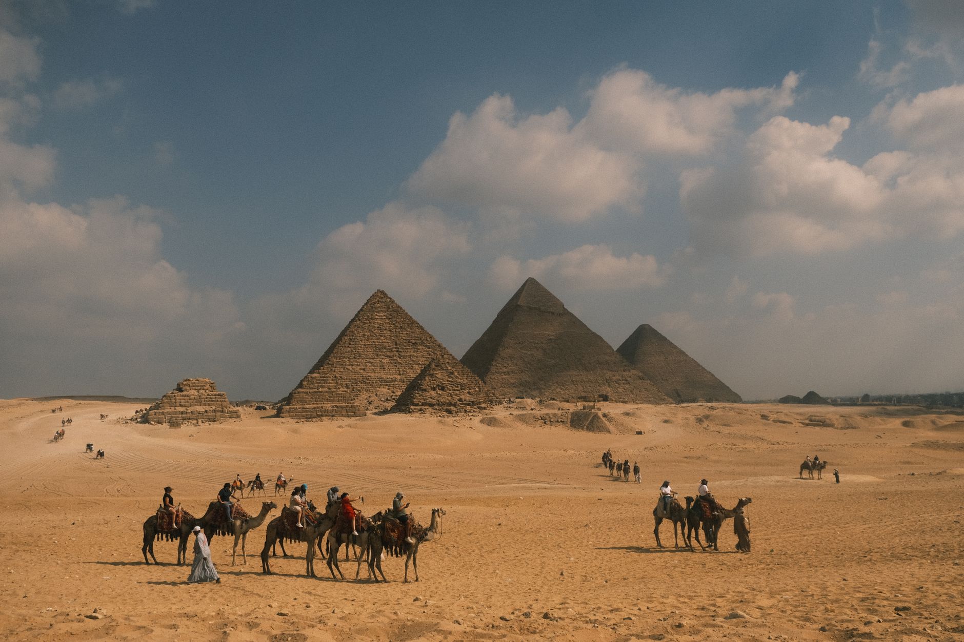 Tourists on camel rides near the iconic Pyramids of Giza under a blue sky.