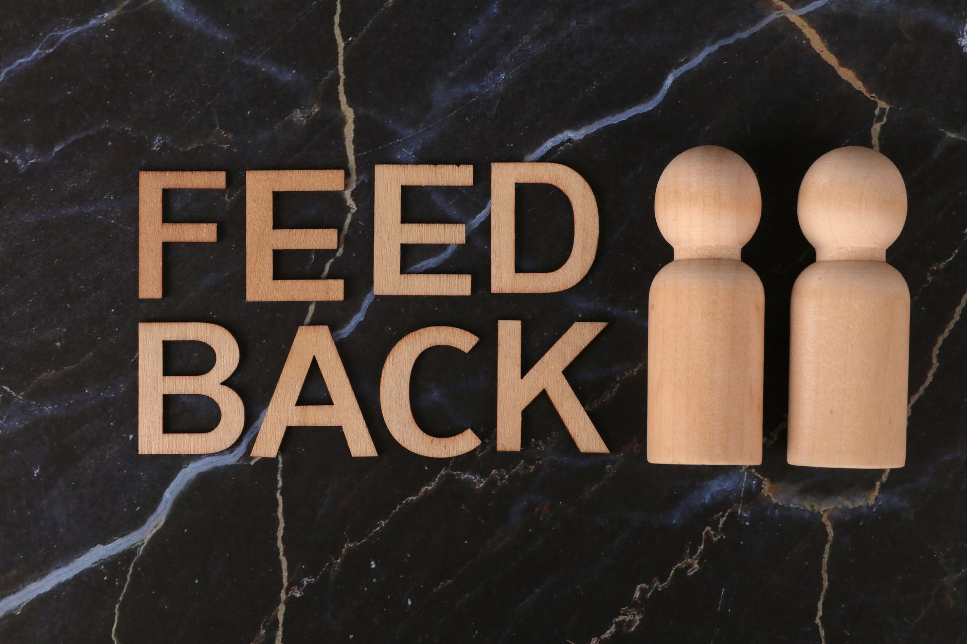 Wooden figures and 'feedback' text on black marble background, symbolizing communication and review.
