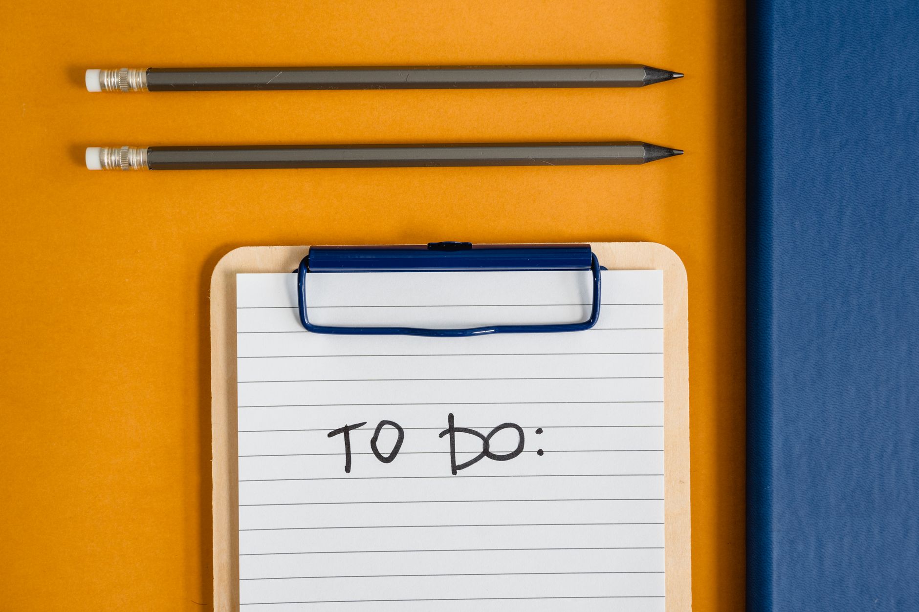 Flat lay of office supplies including a clipboard with a To-Do list, pencils, and a notebook on a yellow surface.