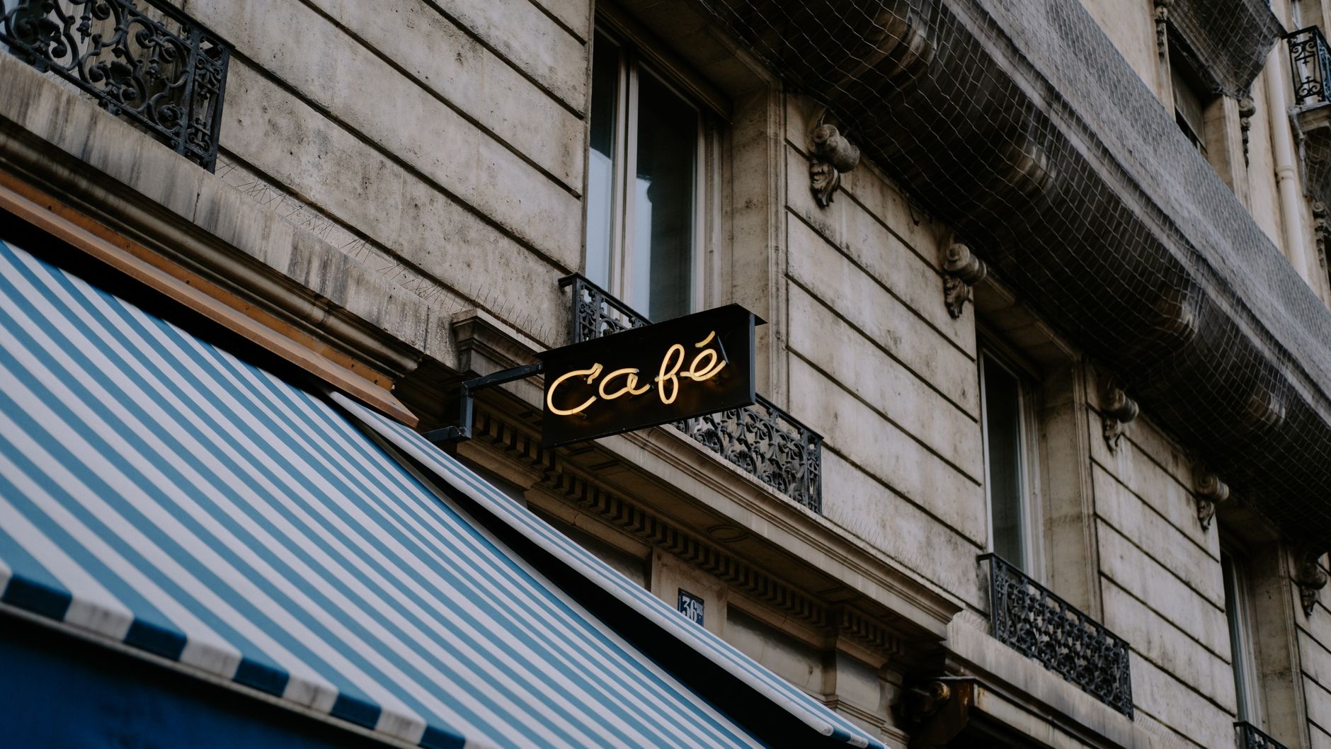 Elegant stone facade featuring a chic café sign and striped awning, enhancing urban charm.