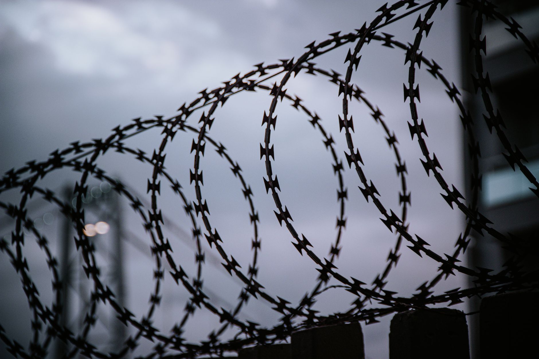 A dramatic view of barbed wire silhouetted against a cloudy sky, capturing themes of security and confinement.