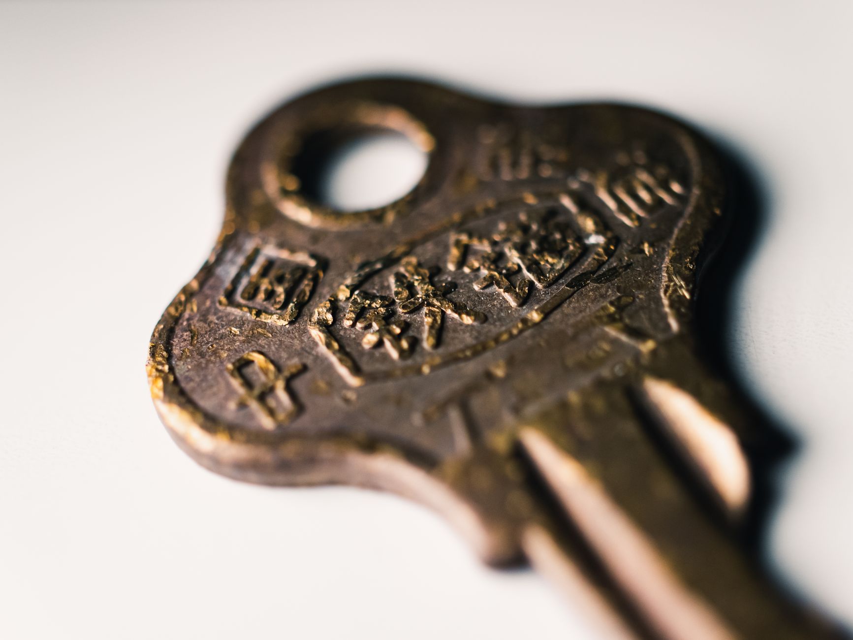 Macro shot of an old brass key featuring worn text on a white surface.