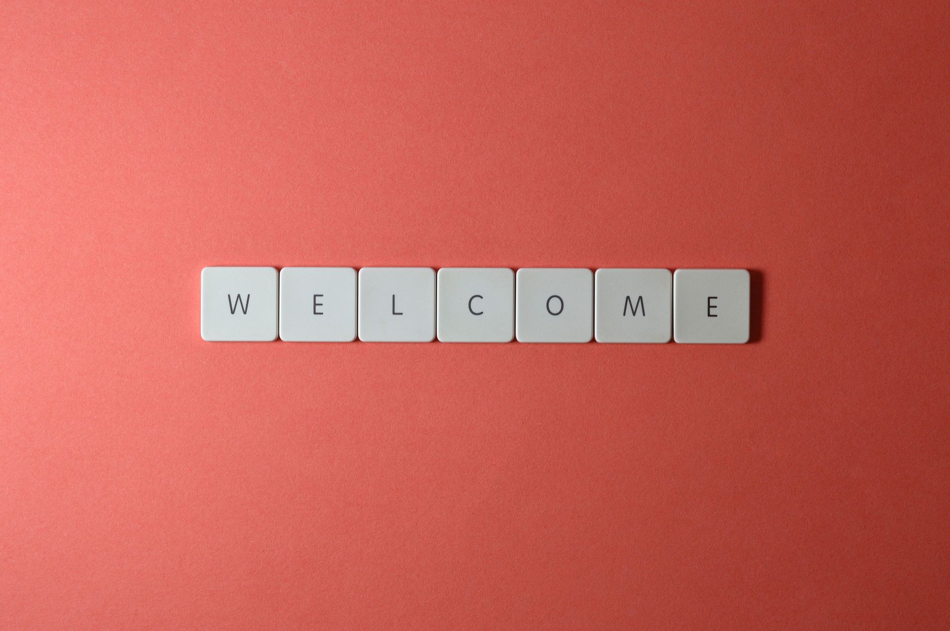 Flat lay of white tiles spelling 'WELCOME' on a red background