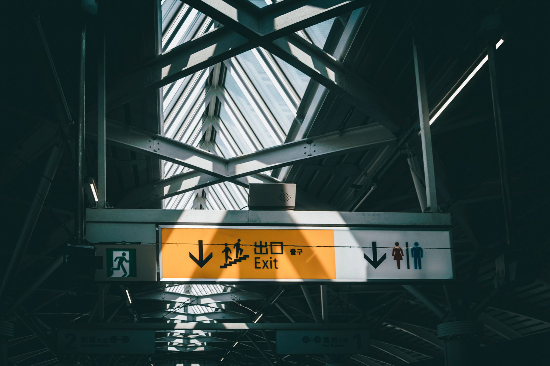 Dramatic indoor shot of a railway station exit sign with skylight above, casting shadows.